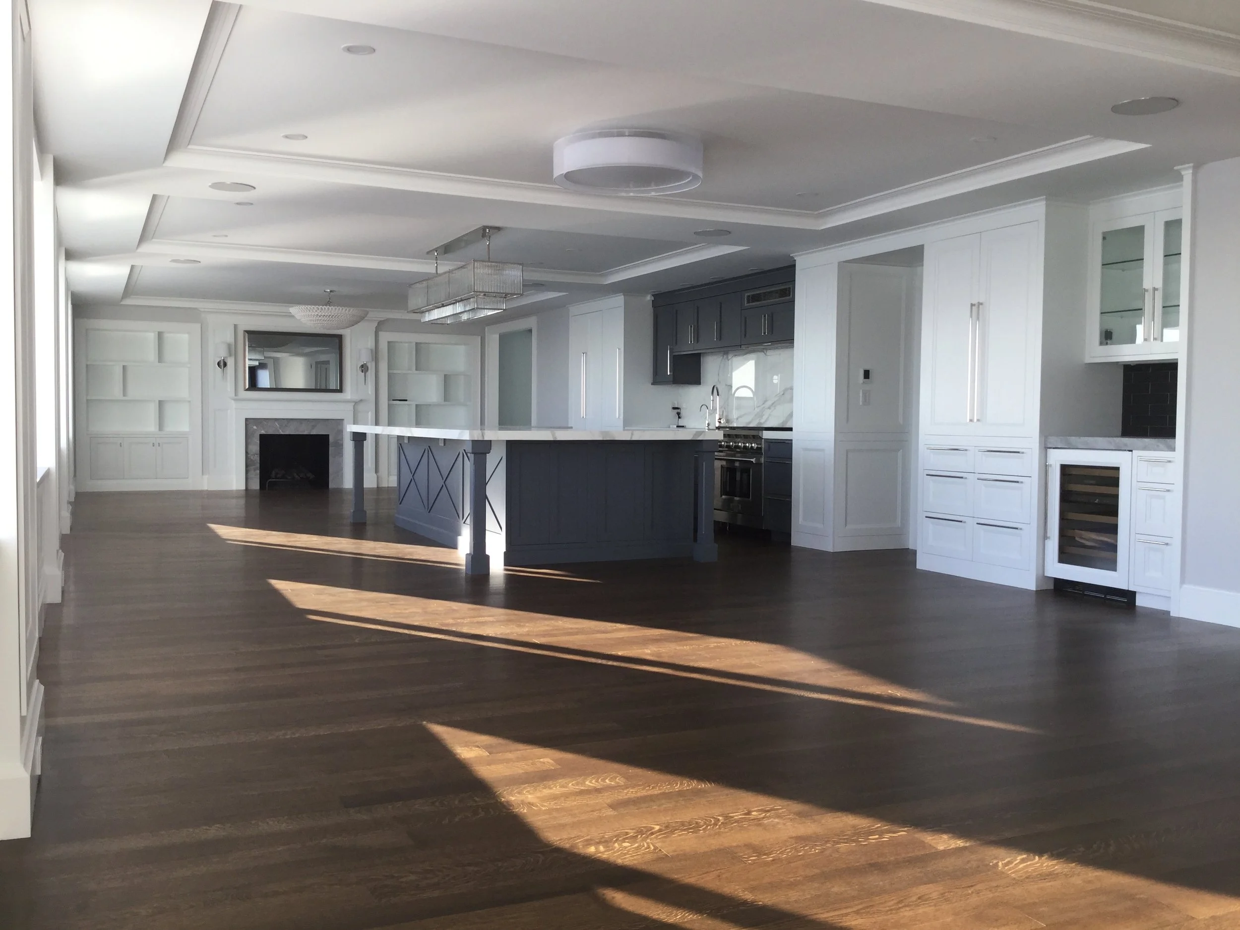 Spacious modern kitchen with white cabinets, dark island, marble countertops, and hardwood floors, illuminated by natural light.