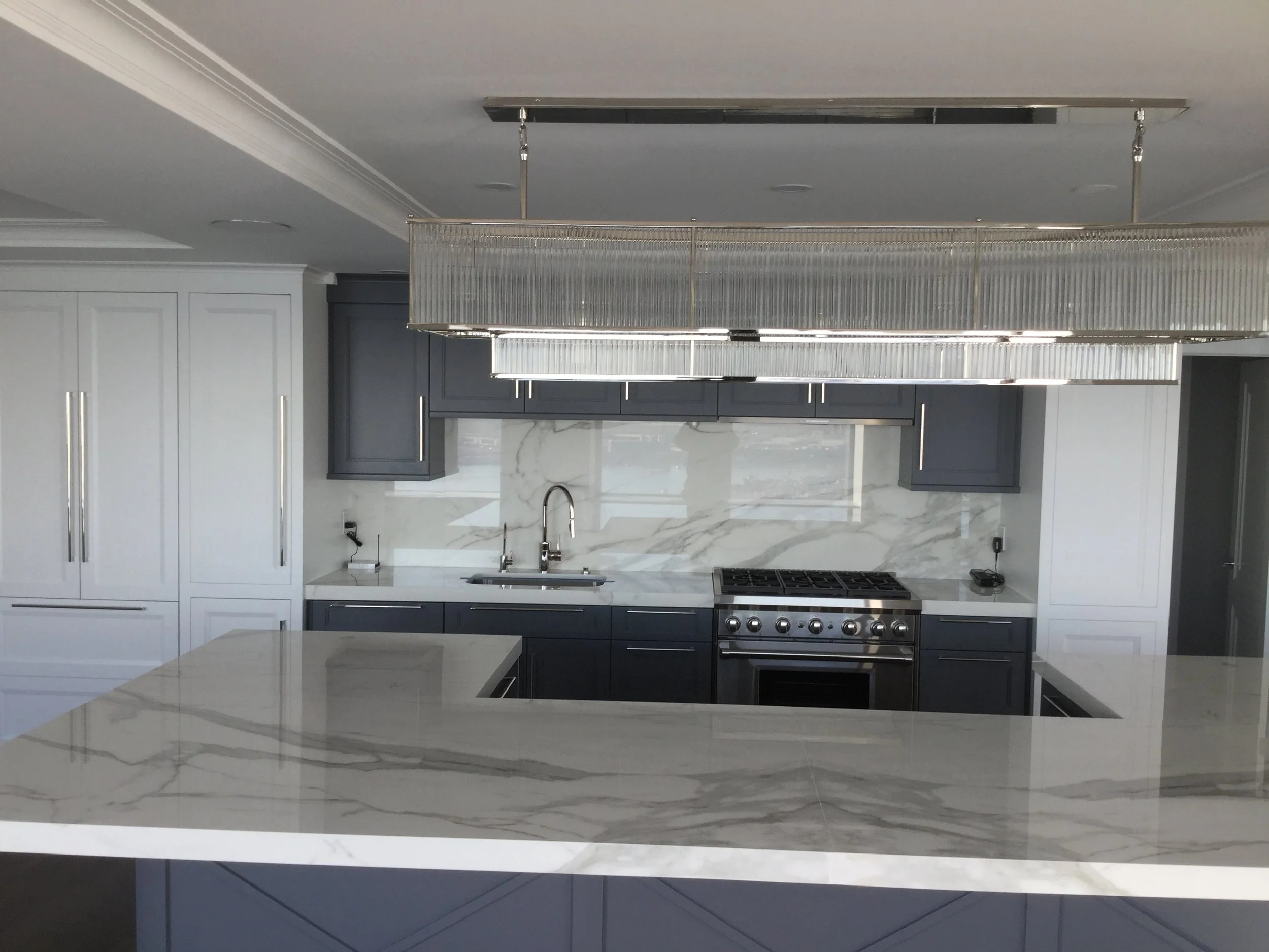 Modern kitchen with gray cabinets, white marble countertops and backsplash, stainless steel stove, and a large island with similar marble surface.