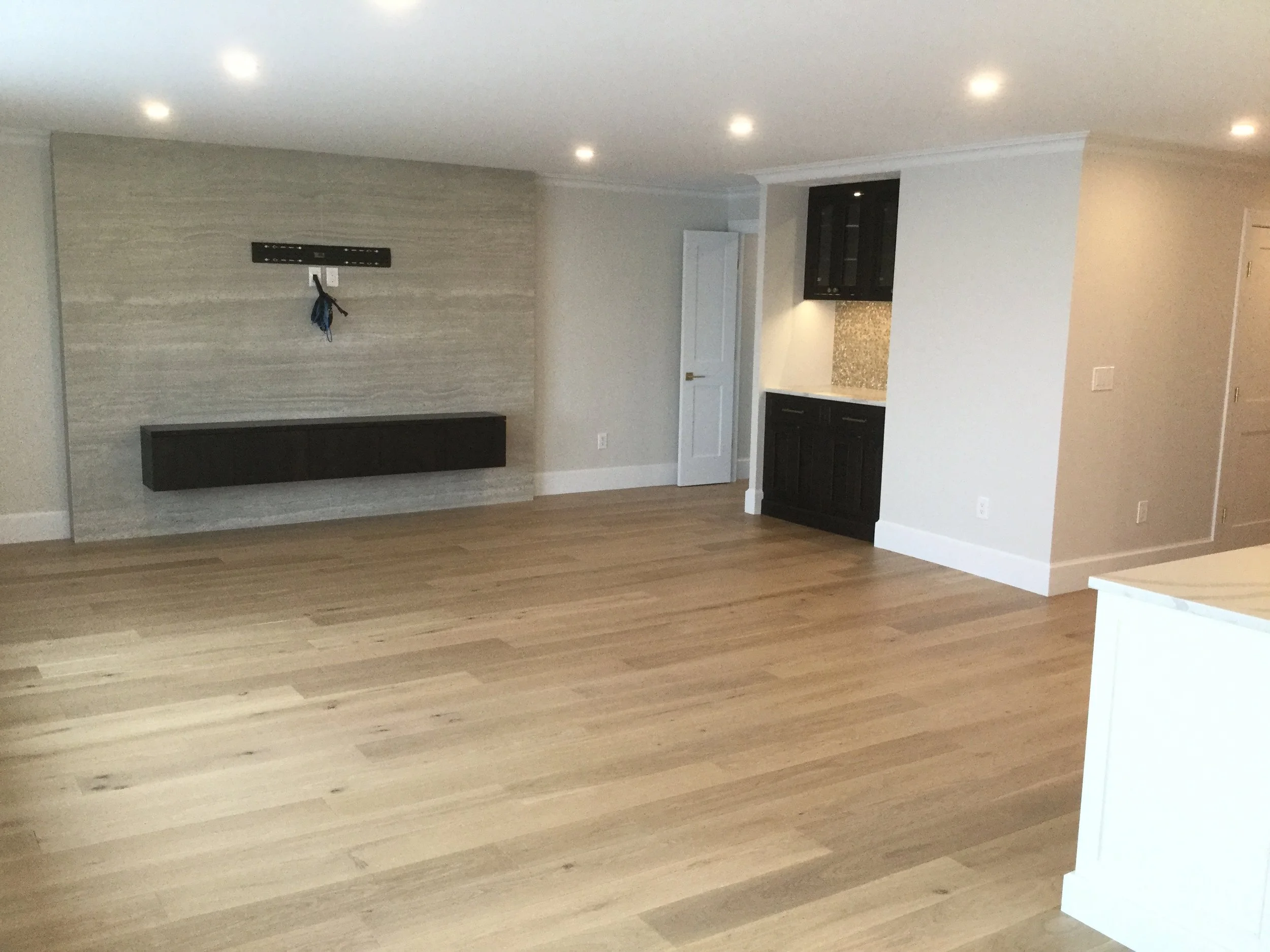 Empty living room with hardwood floors, recessed lighting, and a textured accent wall with a mounting bracket for a TV.