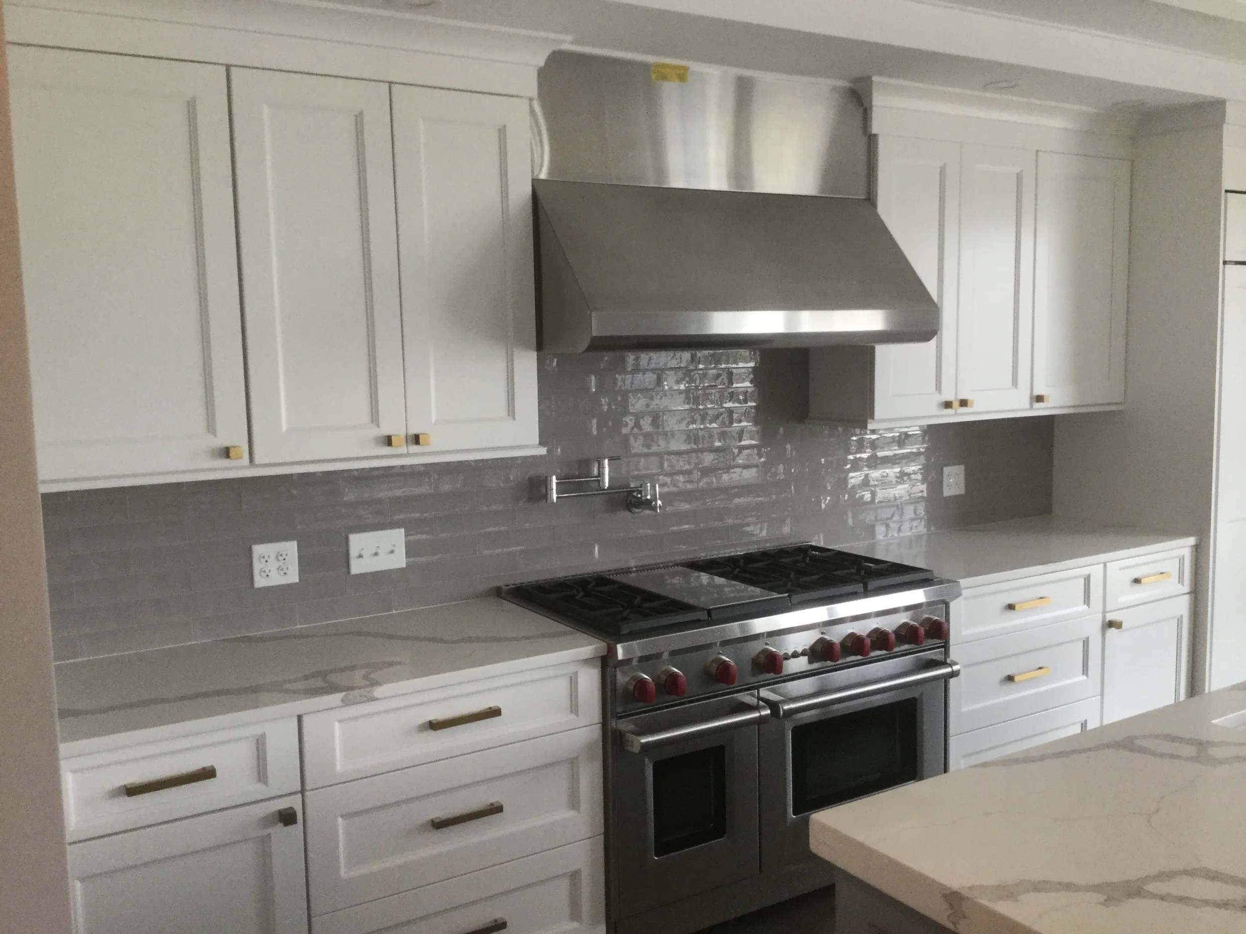 Modern kitchen with white cabinets, gray backsplash, stainless steel range hood, and a stove with red knobs.