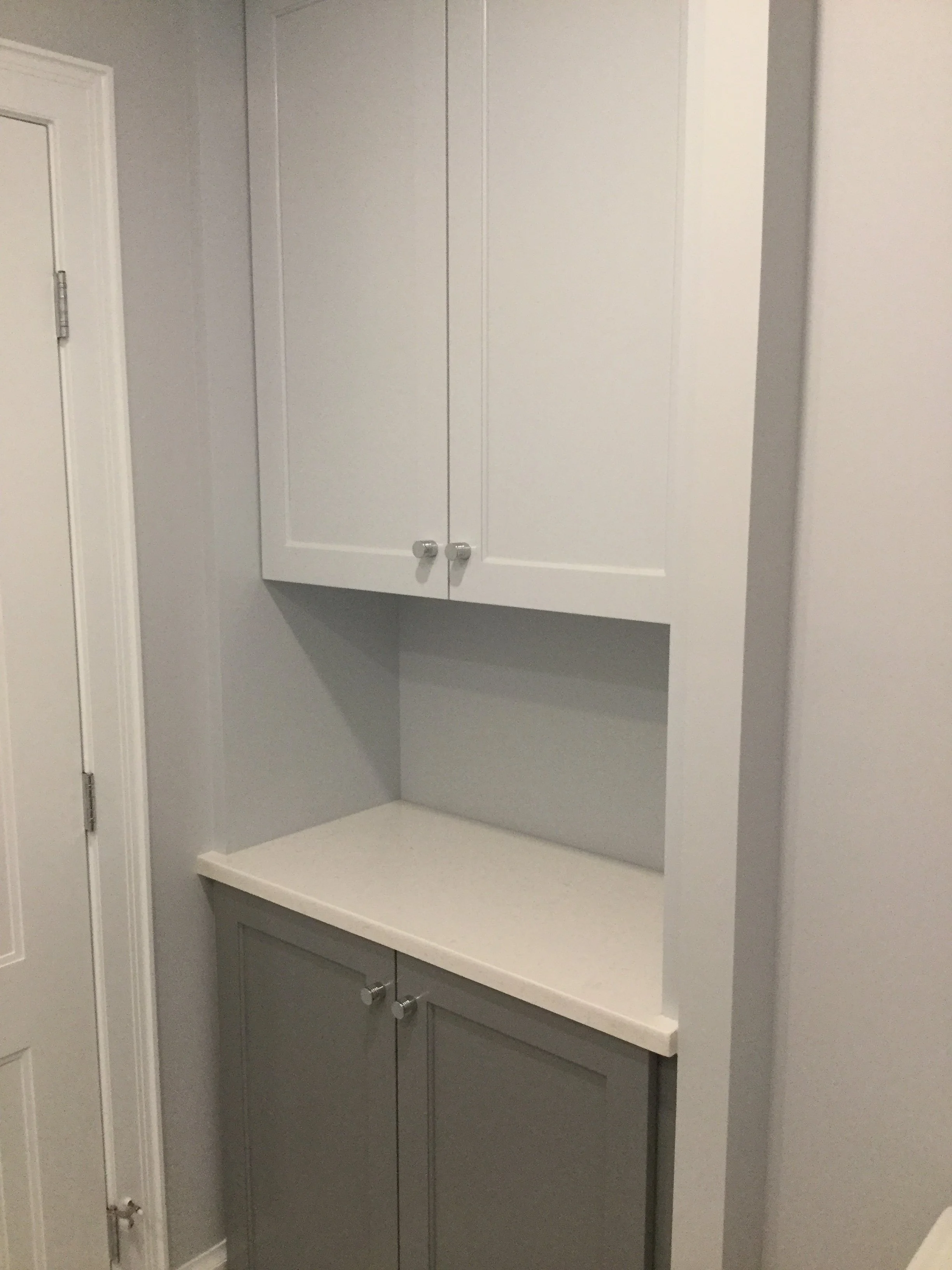 A built-in wall cabinet with two upper doors, a countertop, and two lower doors, all painted in white and gray.