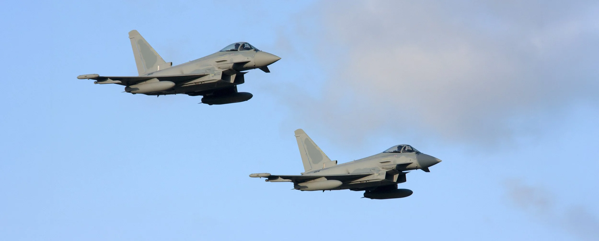 Two fighter jets flying in formation against the sky with some clouds.
