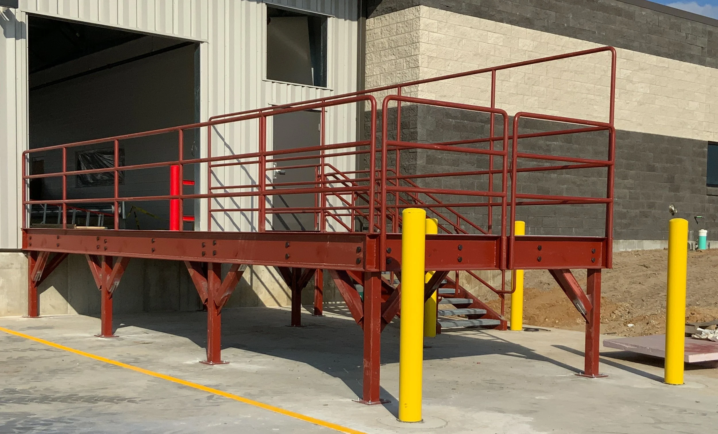 Steel loading dock platform with stairs, railings, and safety bollards fabricated for commercial facility.