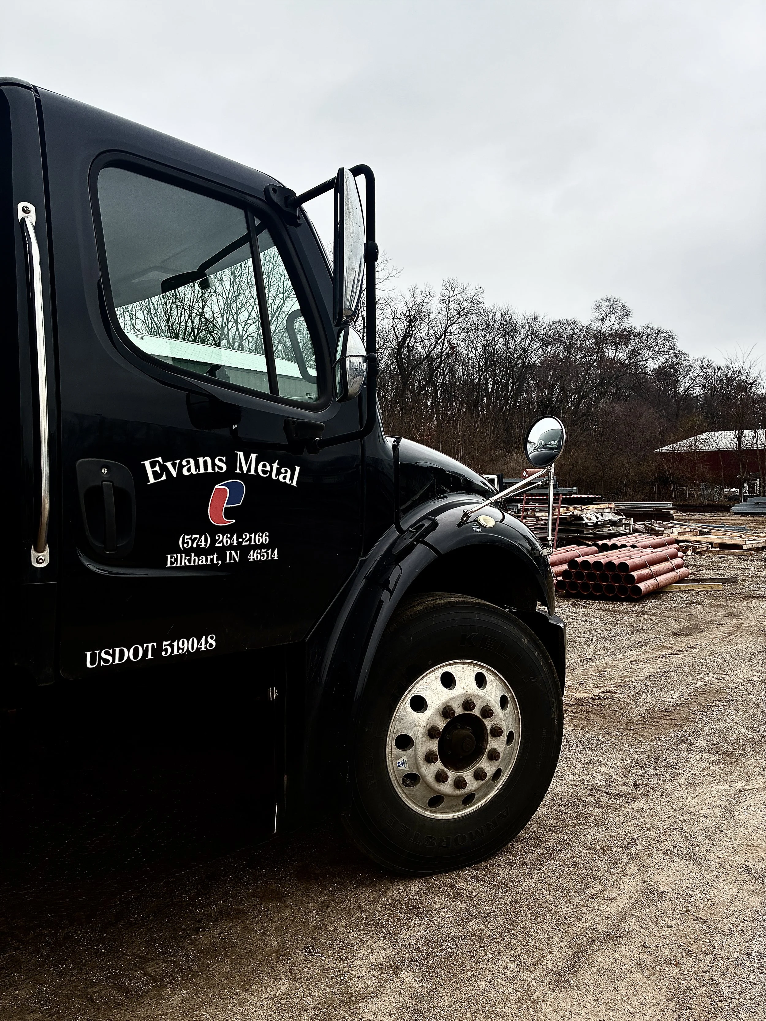 Evans Metal Products company truck parked at the fabrication shop with steel pipe material visible in the yard.