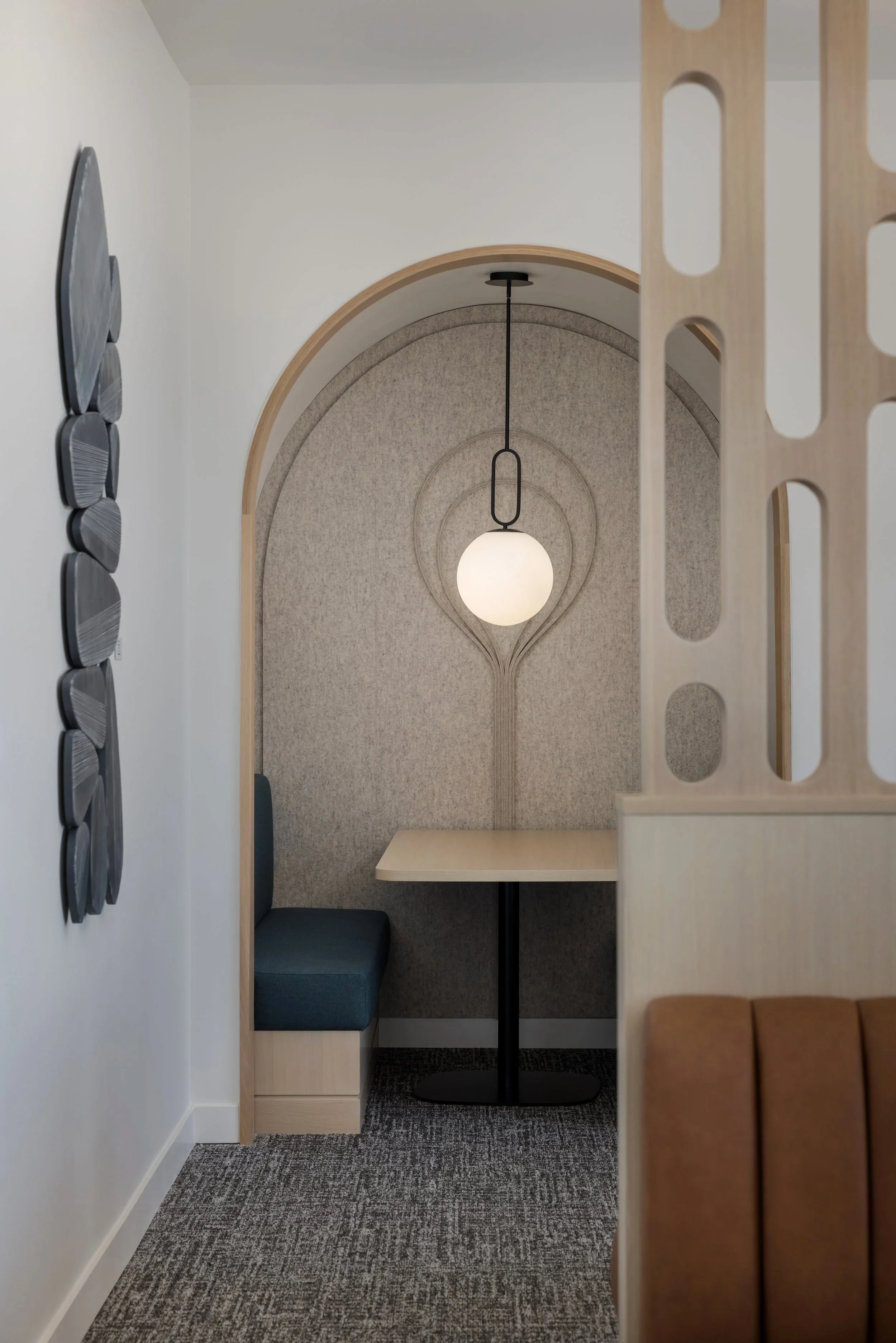 A cozy dining nook with a small table, a bench with teal upholstery, and a hanging globe light fixture in an arched alcove with textured wallpaper.