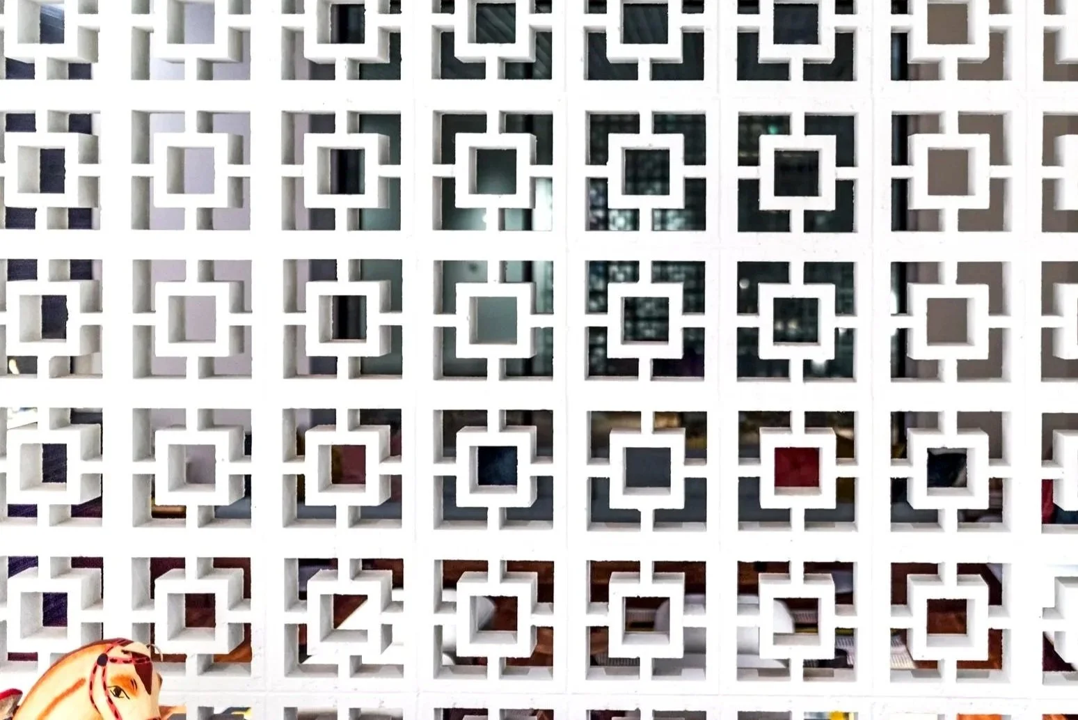 Close-up view of a decorative white wall with a geometric pattern of square cutouts, showing some objects and the interior behind the wall.