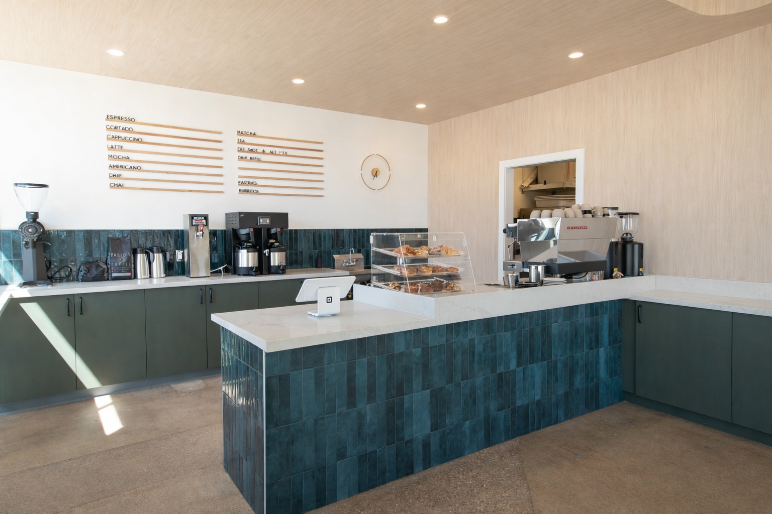Coffee shop counter with coffee machines, pastries, and a menu on the wall.