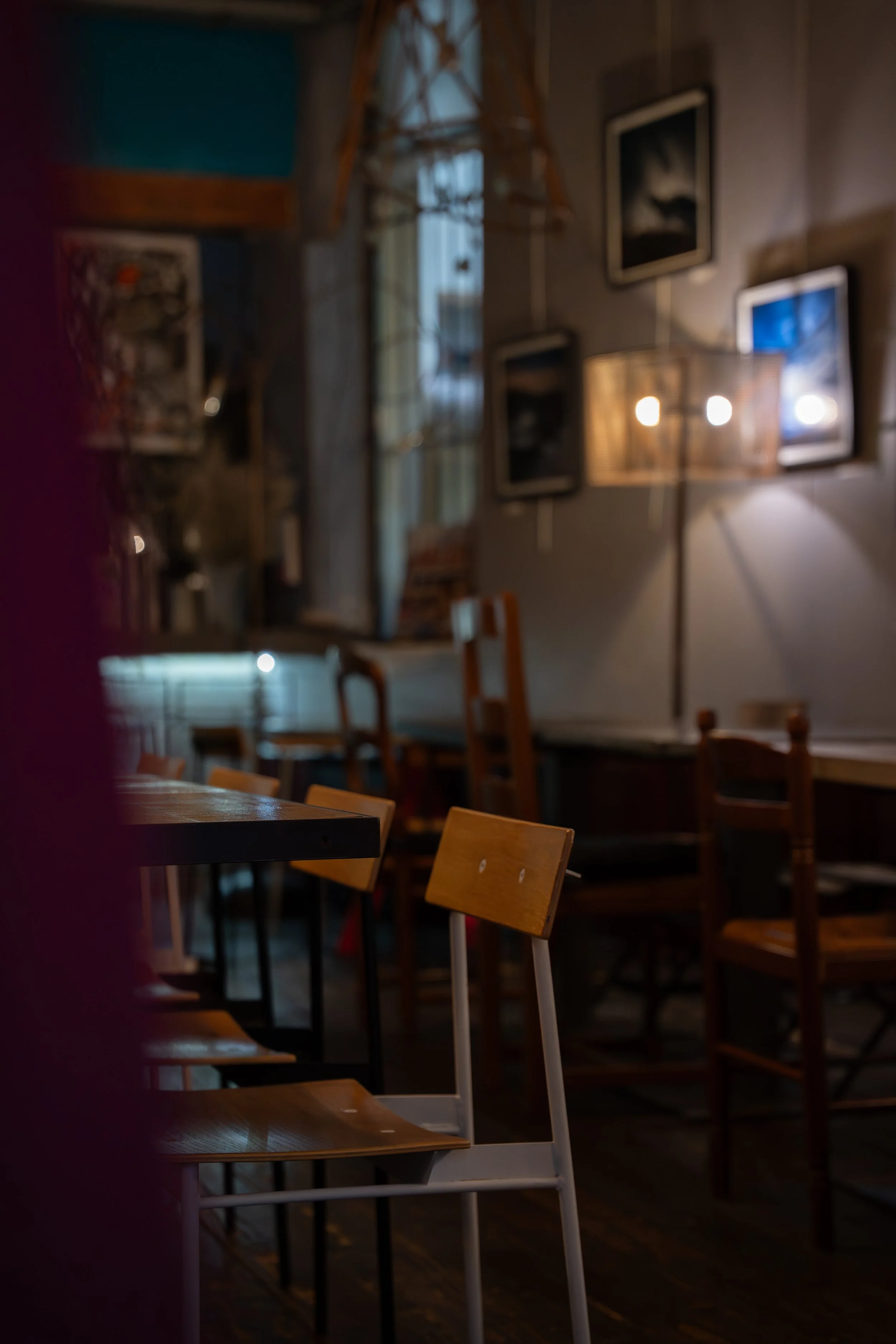 Intérieur d'un café ou restaurant avec des chaises en bois, tableaux et éclairage doux, ambiance chaleureuse et cosy.