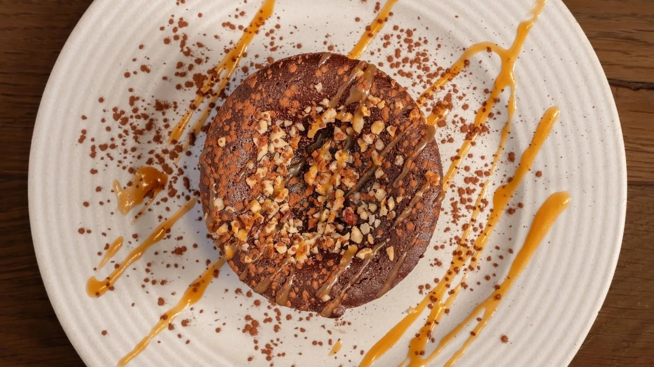 Gâteau au chocolat décoré de noisettes hachées, avec des traites de caramel et de chocolat en décoration sur une assiette blanche