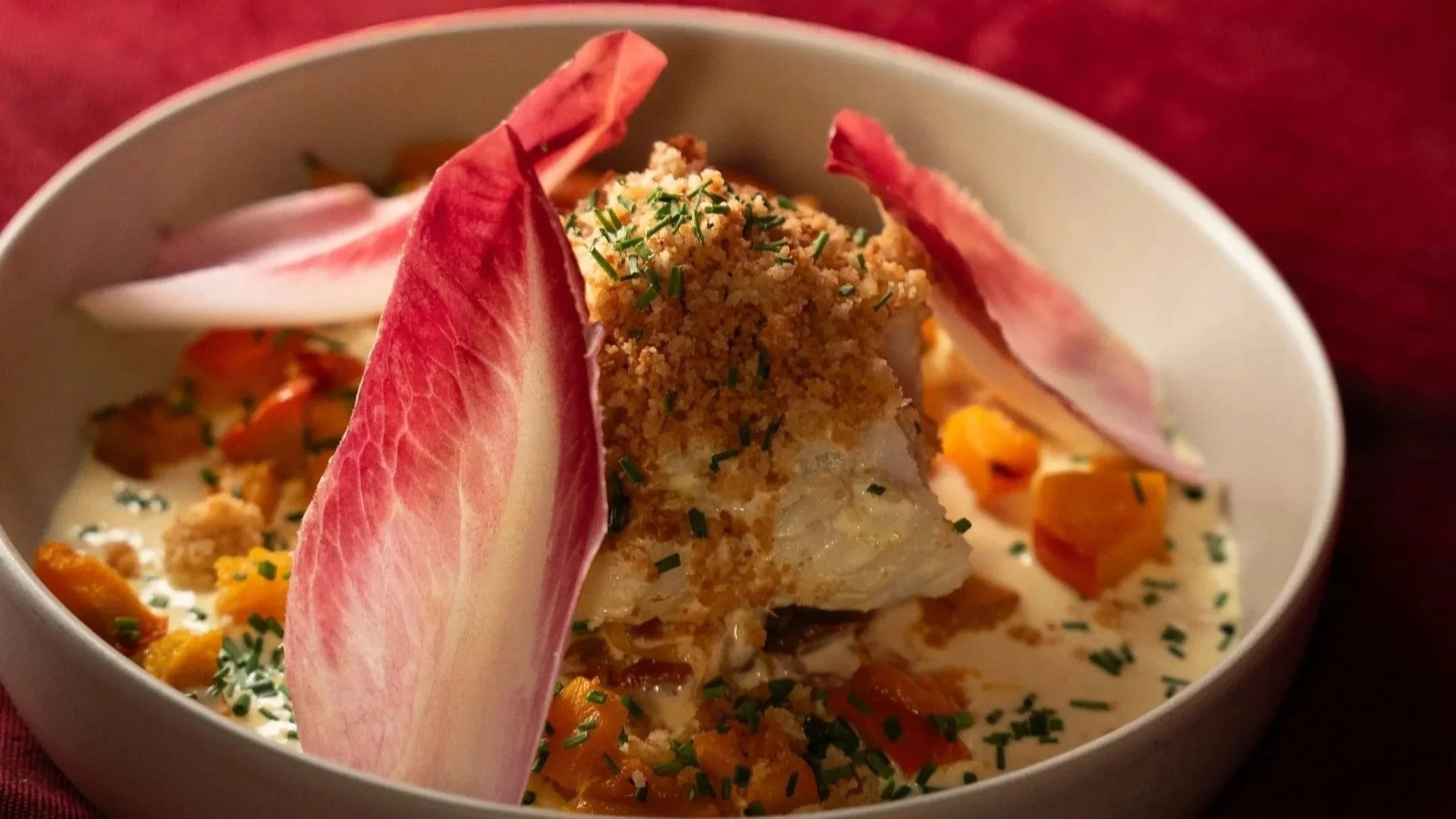 Plat de poisson en sauce avec légumes, garnitures croustillantes et feuilles de radis