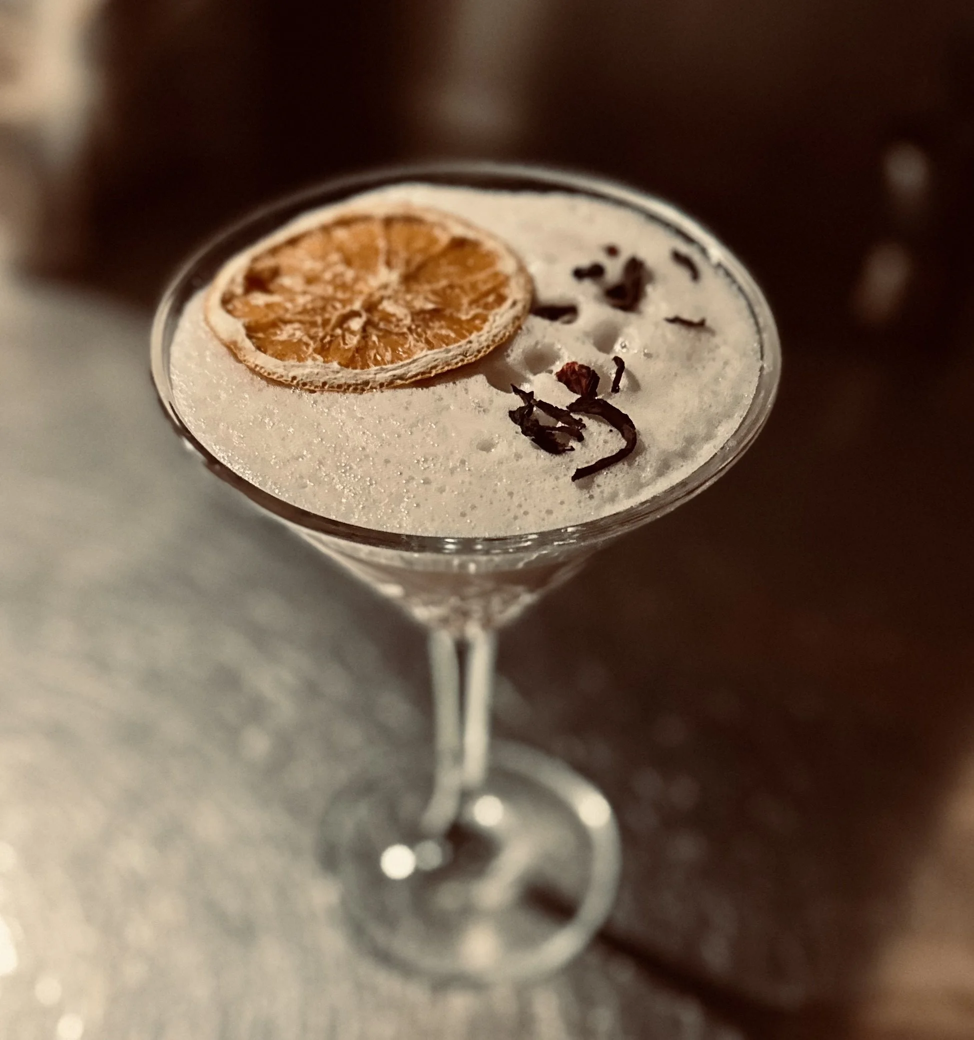 Un cocktail dans un verre à martini avec une tranche de citron séchée et des copeaux de chocolat sur le dessus.