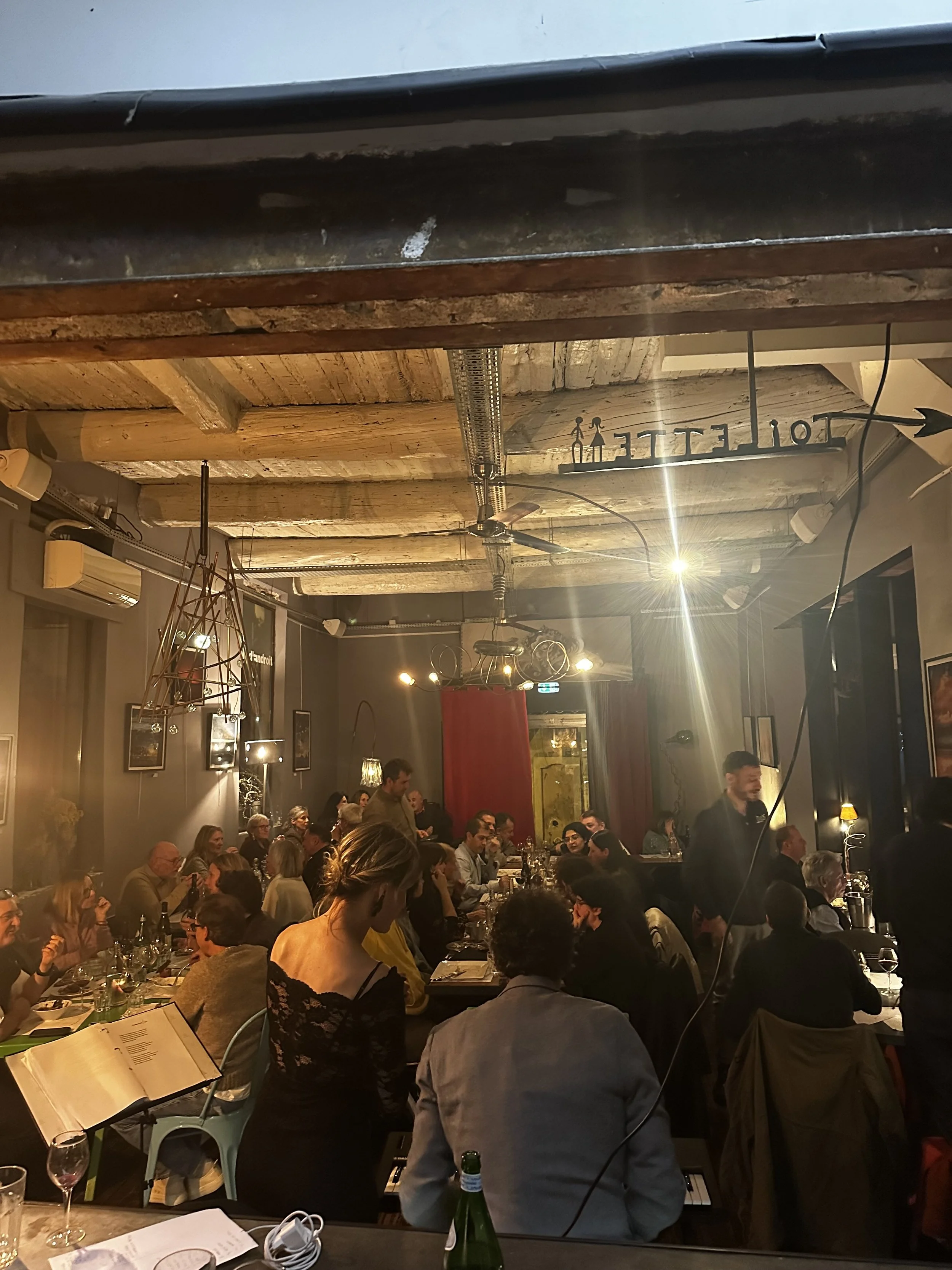 Une réunion ou un dîner dans un restaurant avec plusieurs personnes assises autour d'une grande table, ambiance chaleureuse avec décoration intérieure en bois et lumières tamisées.