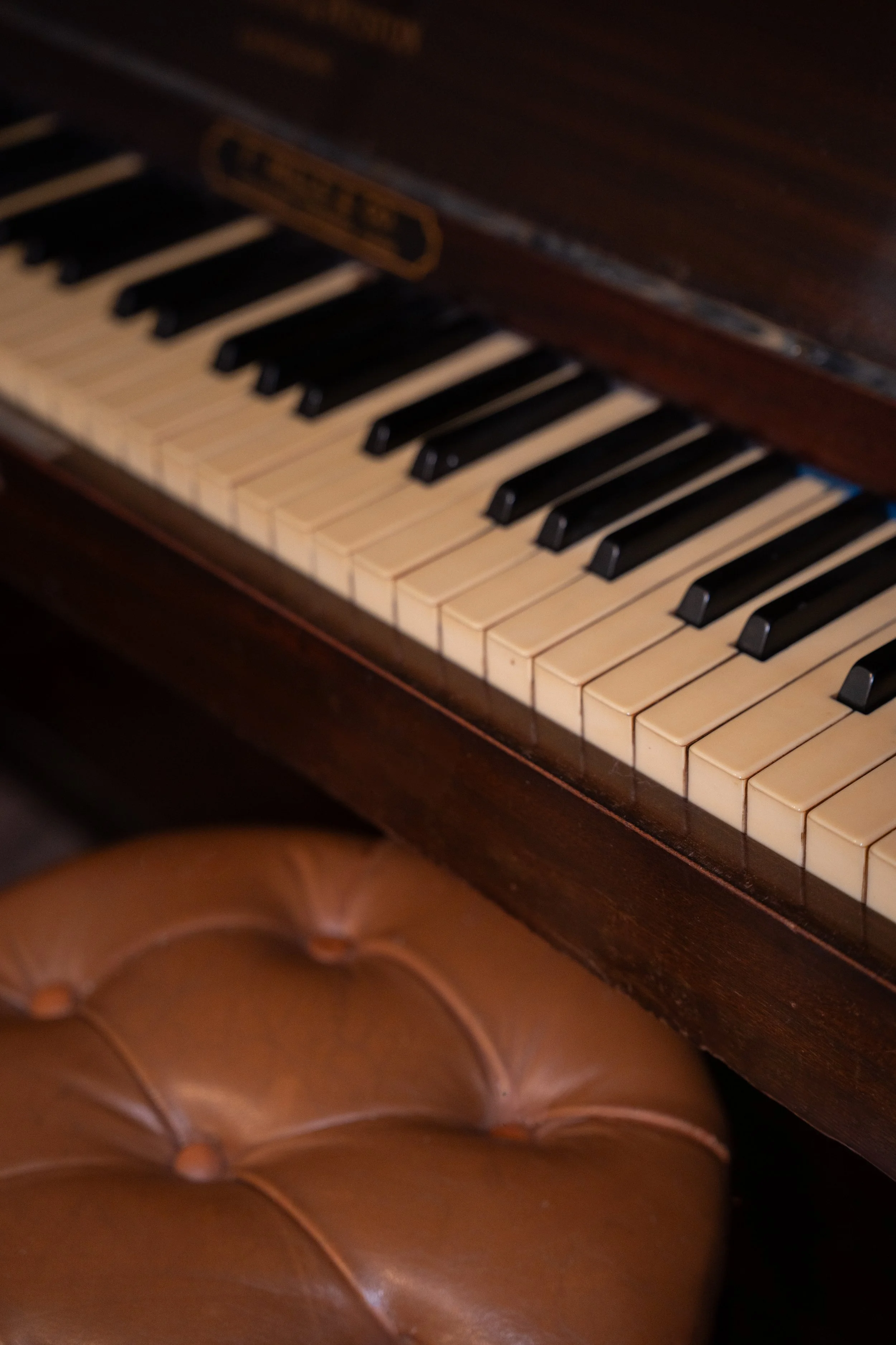 Clavier de piano en bois sombre avec touches blanches et noires, partiellement visible, avec un tabouret en cuir marron en dessous.