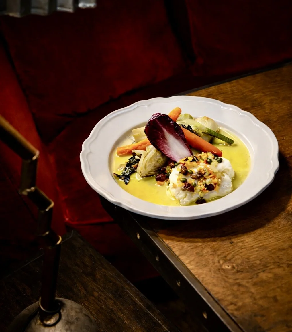 Assiette de légumes crus avec une sauce et des graines, présentée sur une table en bois dans un cadre avec chaise rouge.