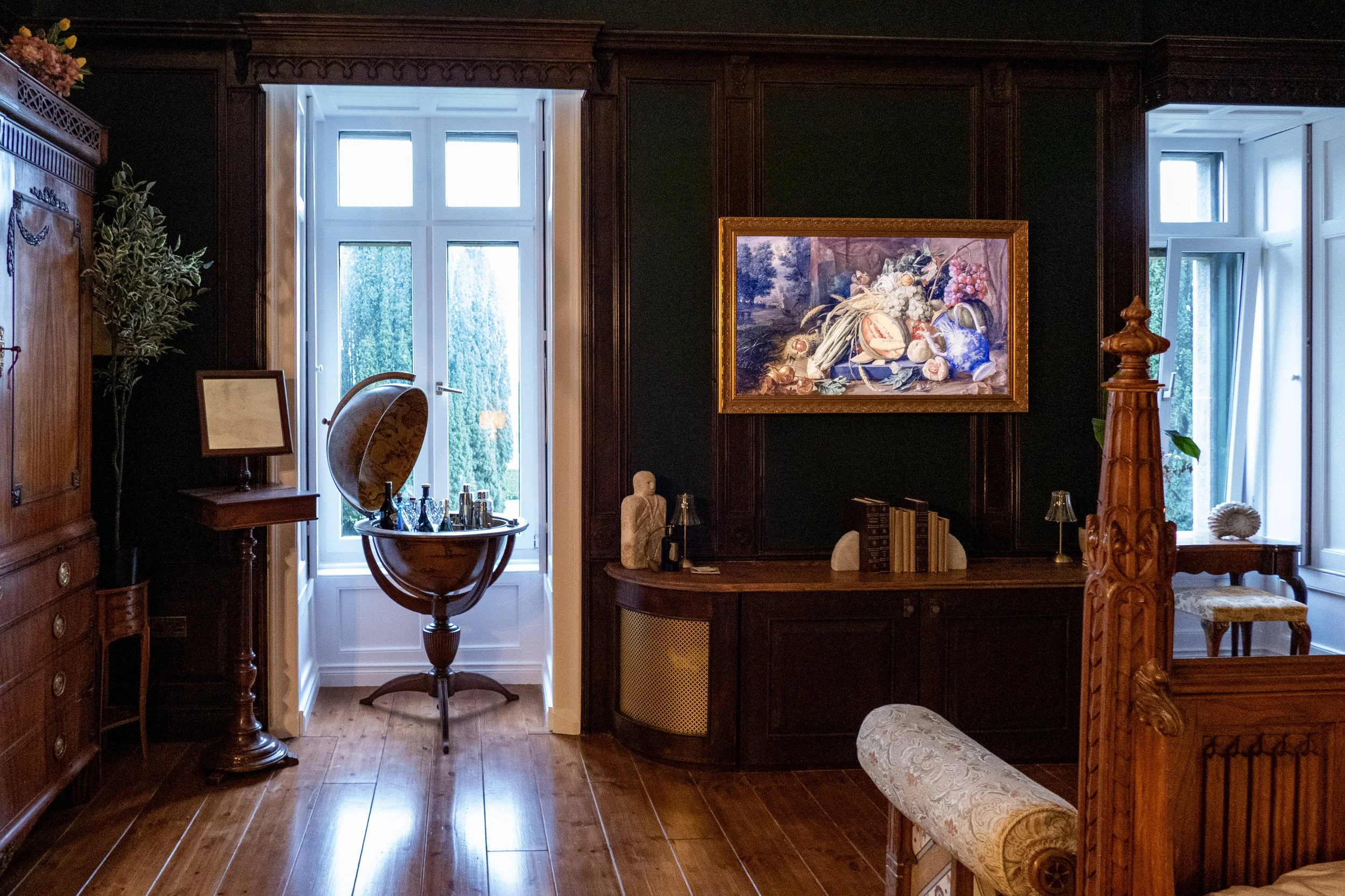 Interior of a vintage-style room with wooden furniture, a large window, and framed artwork above a sideboard.