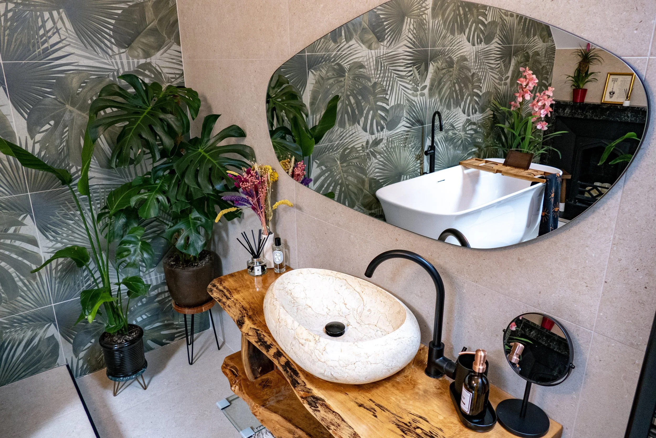 Bathroom with a rustic wooden vanity, a stone sink, a large leaf-patterned wall mirror, and lush green plants.