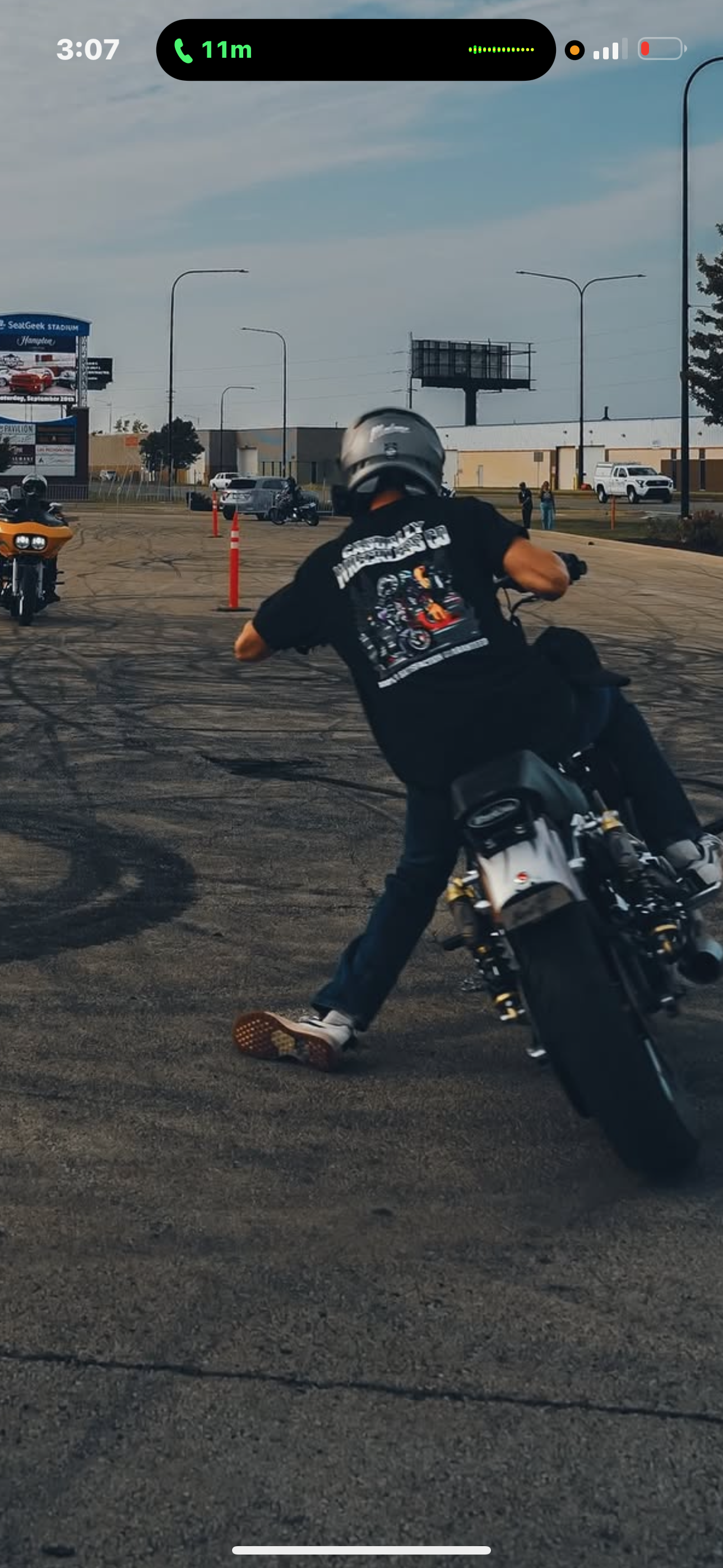 Motorcycle rider performing a burnout in a parking lot with motorcycle tire smoke, wearing a helmet and casual clothes with a Harley-Davidson shirt.