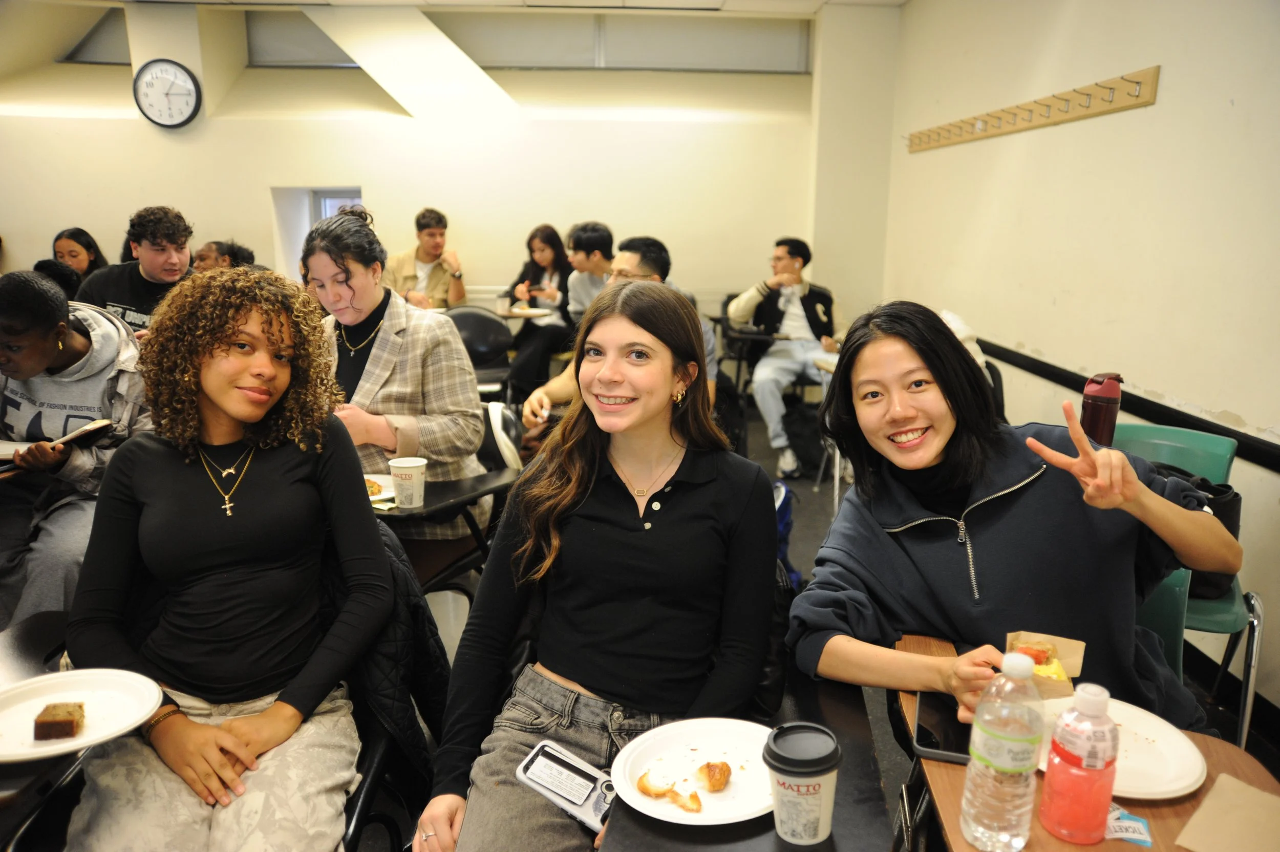 Diverse group of students smiling together in a classroom with plates of food and drinks.