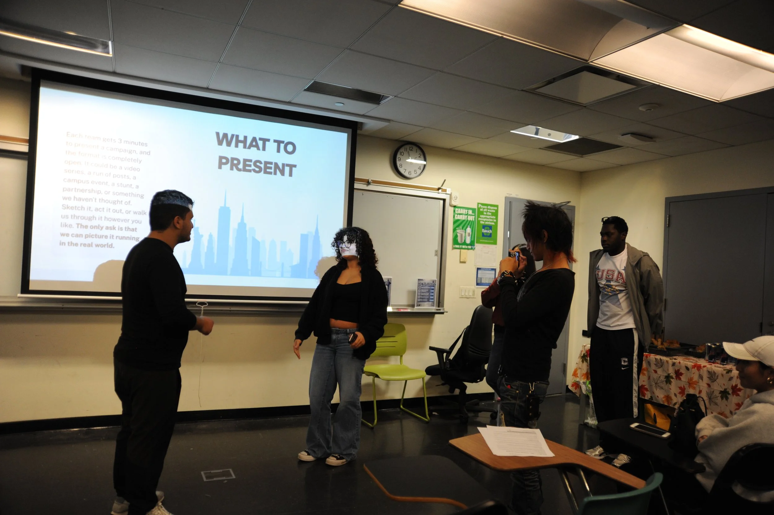 Students perform a presentation in a classroom beside a projected slide titled “What to Present.”