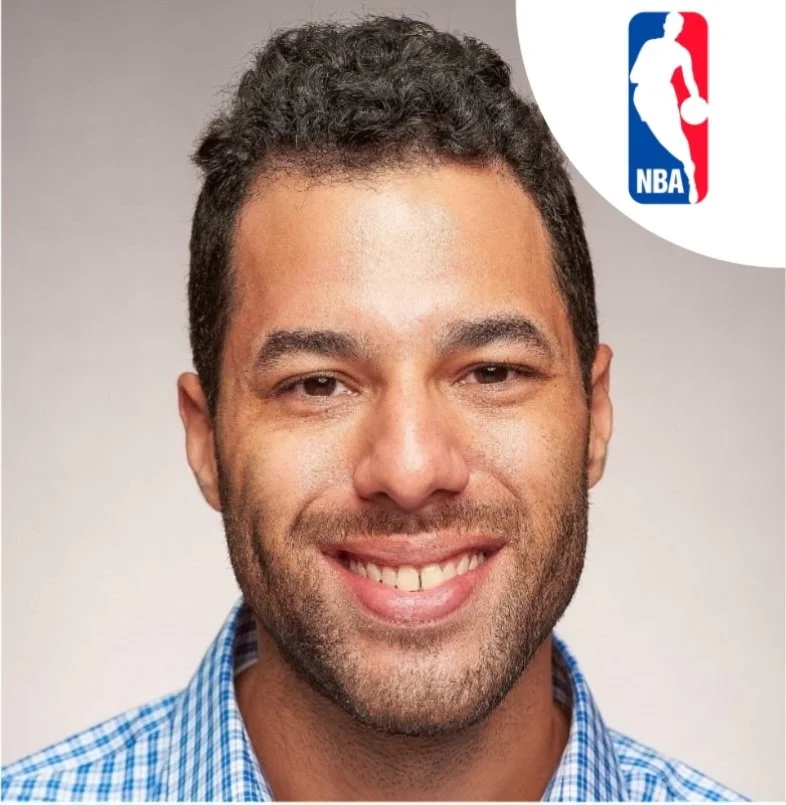 Close-up portrait of a smiling man with short dark hair, wearing a blue checkered shirt. NBA logo is in the top right corner.