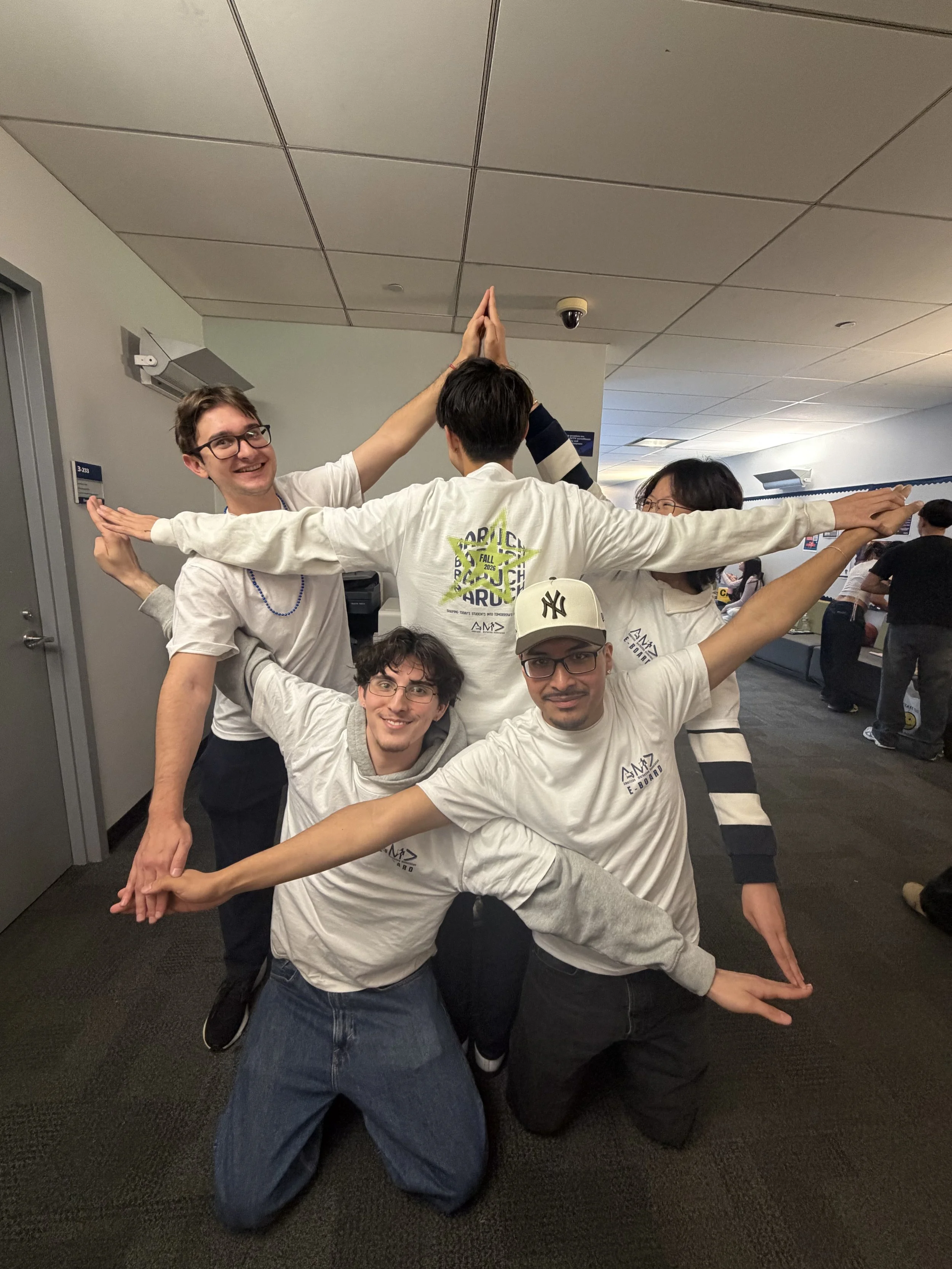 Group of young people creating a human pyramid in an indoor setting, smiling and posing for the camera.