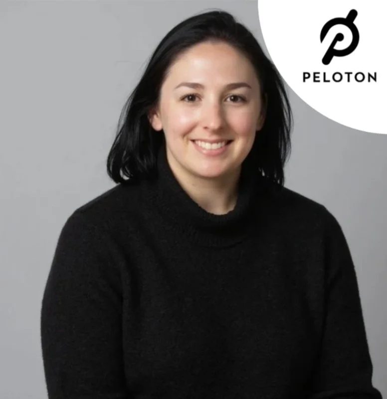 A woman smiling with black hair, wearing a black turtleneck sweater, against a gray background with the Peloton logo in the top right corner.