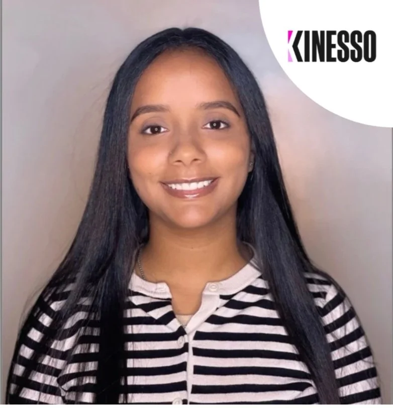 A young woman with long black hair smiling, wearing a black and white striped shirt, indoors with a plain background and a KINESO logo in the top right corner.