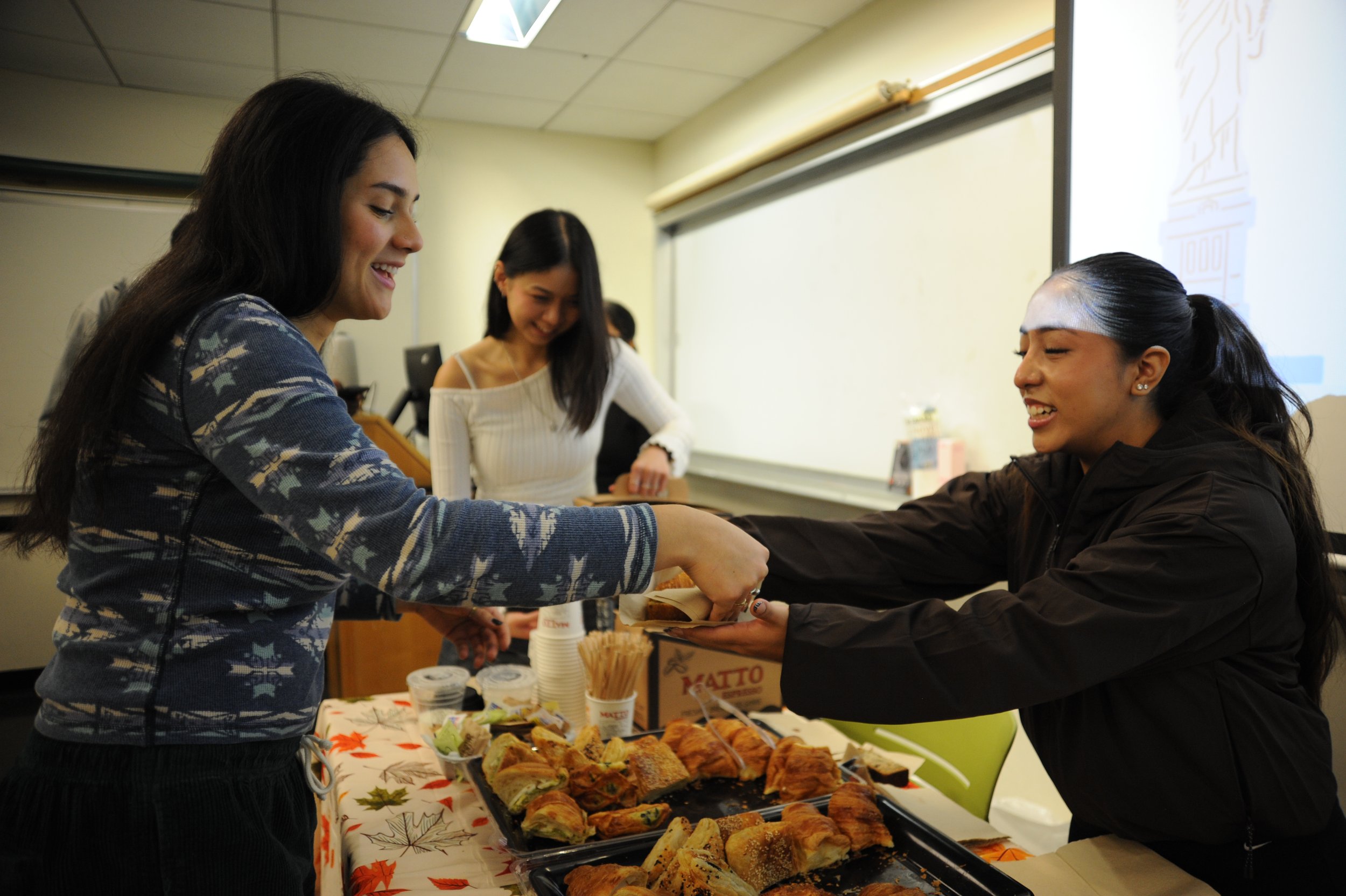 Three women share food at a classroom table during a catered gathering.