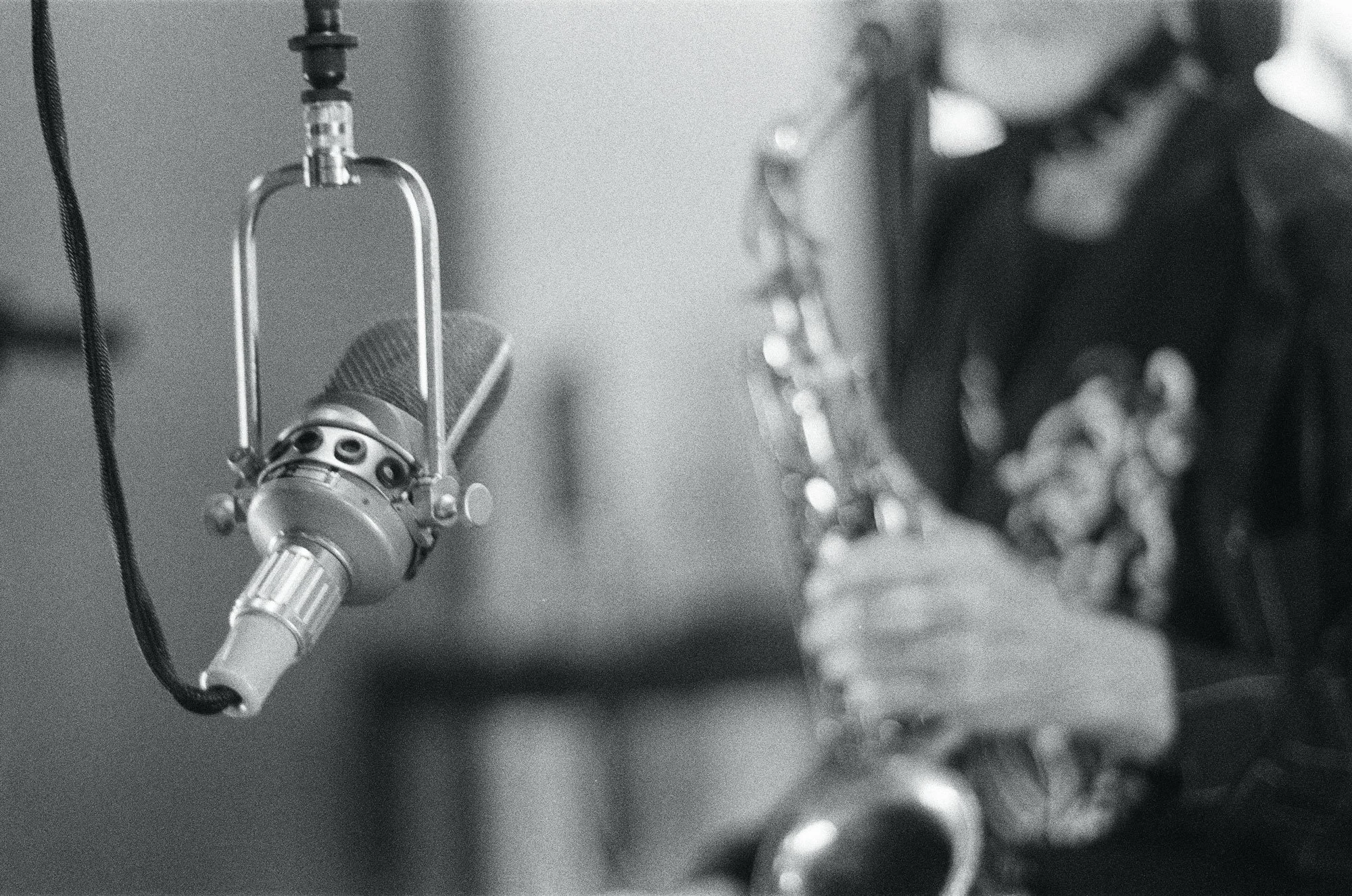 Close-up of a microphone on a stand in a recording studio with a blurred person in the background.