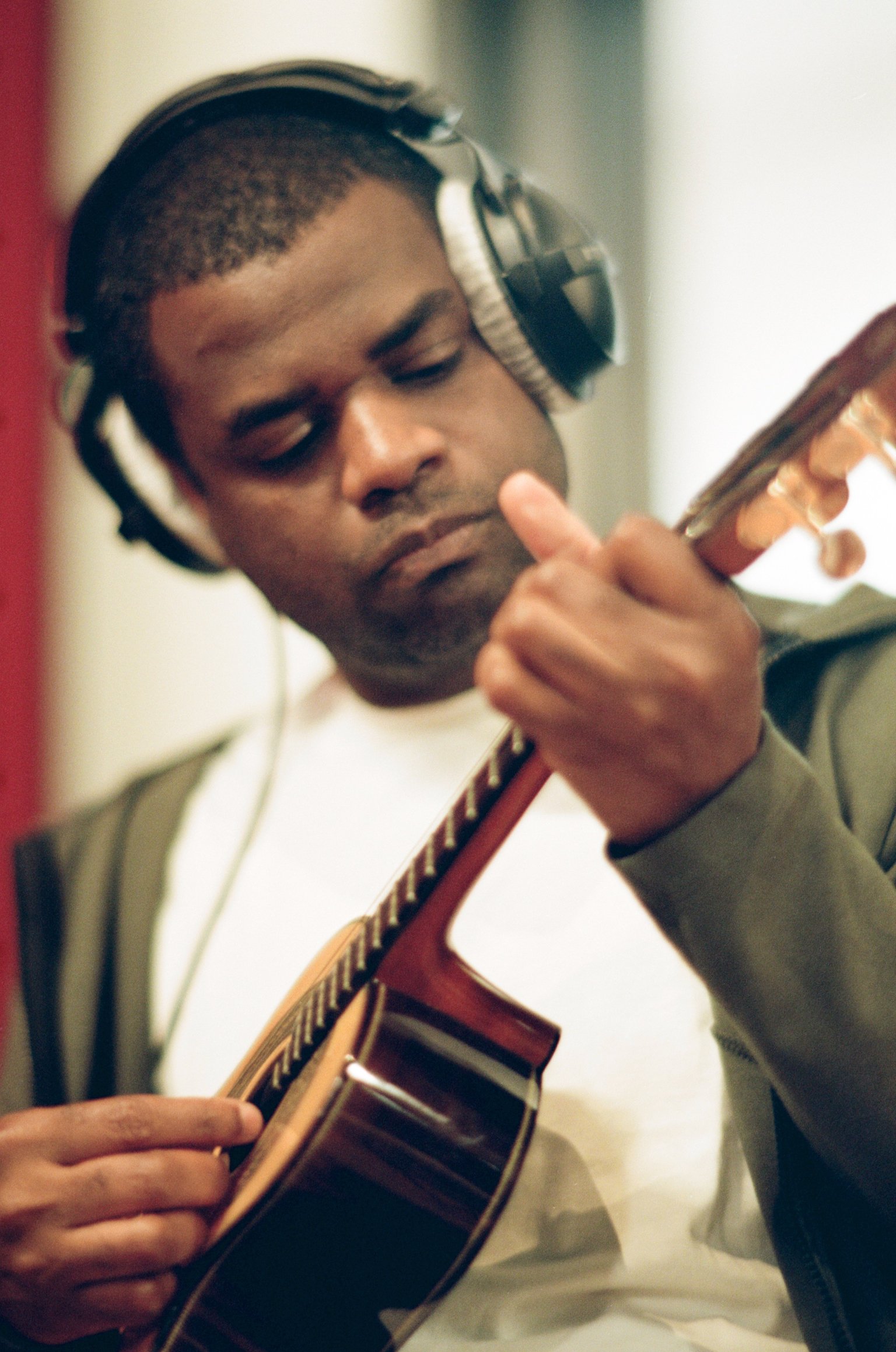 A young man with short hair and wearing headphones playing an acoustic guitar.