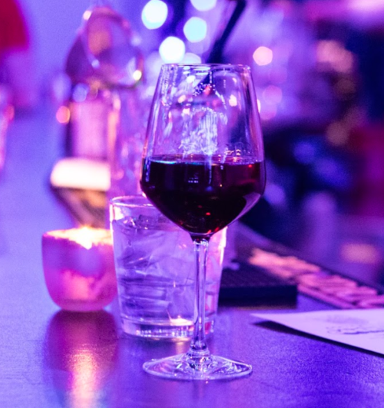 A glass of red wine and a glass of water on a bar or table with purple and blue lights in the background.