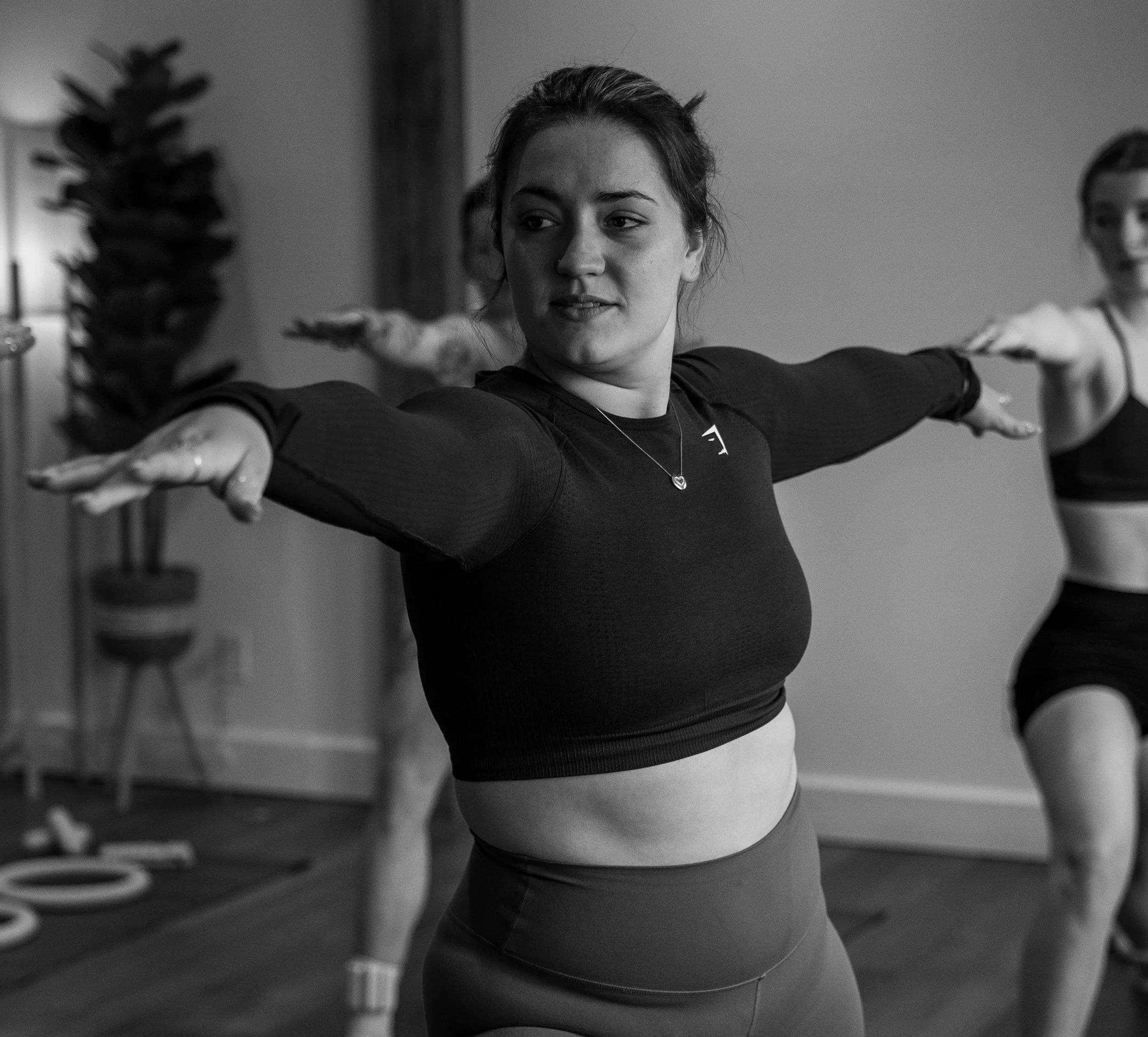 A woman practicing yoga or stretching indoors, with her arms extended and a focused expression.