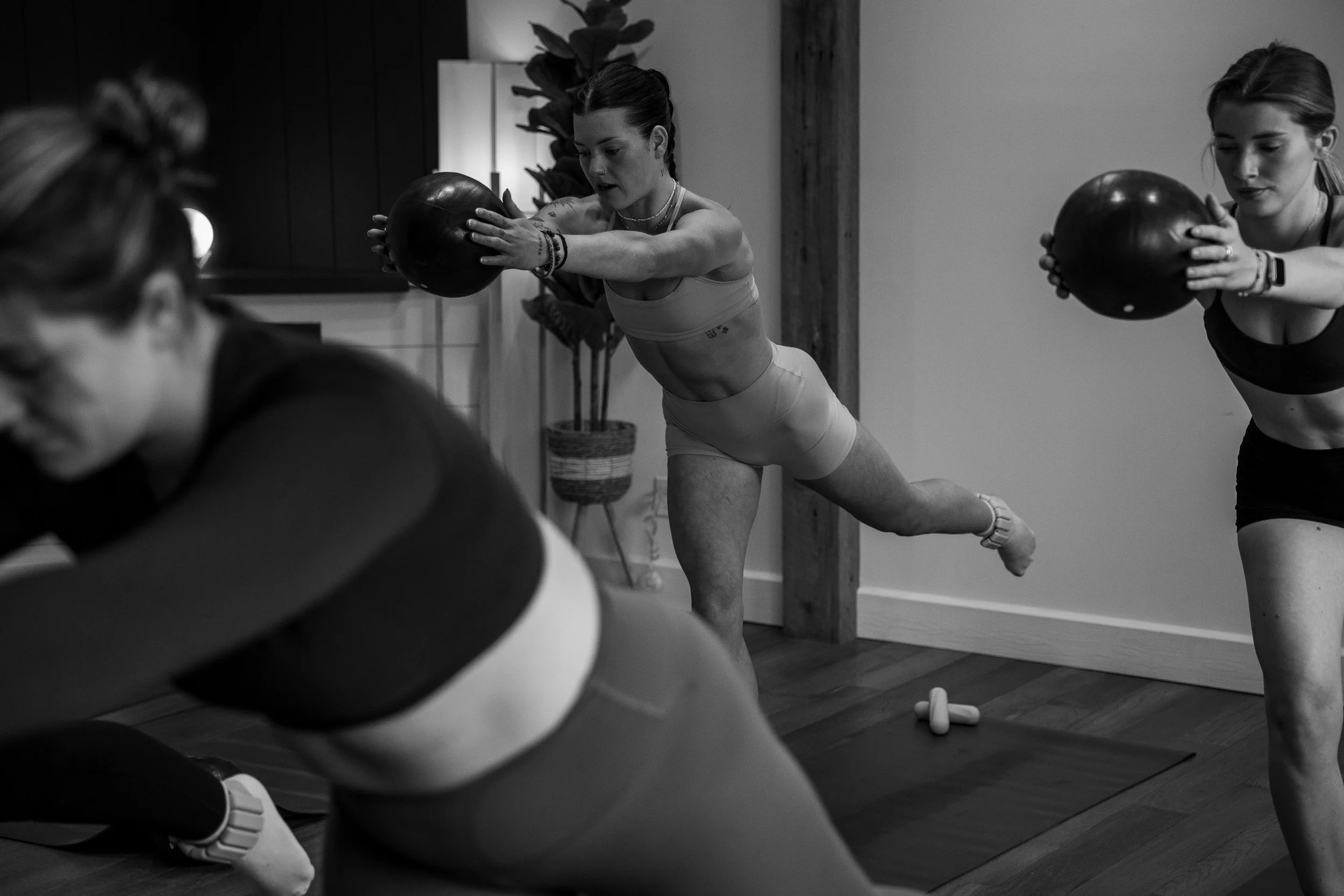 Women participating in a fitness class lifting kettlebells in a gym with wooden floors and walls.