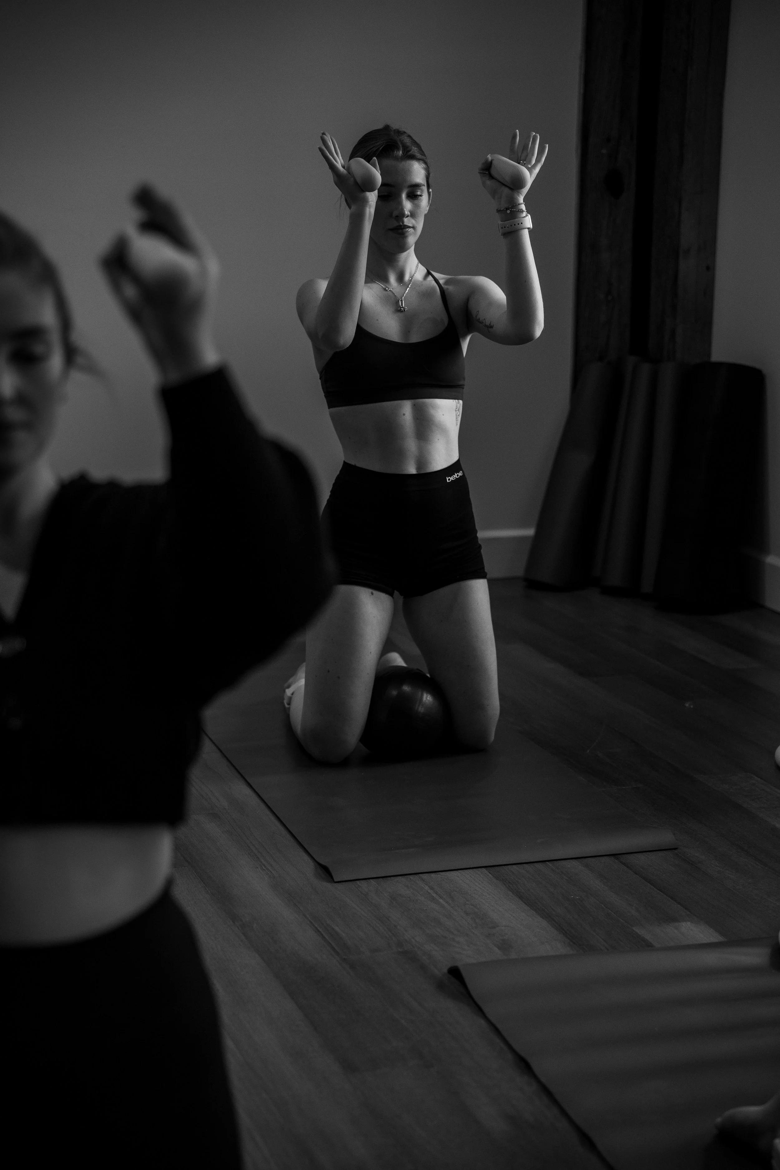 A woman practicing yoga or meditation kneeling on a yoga mat with her eyes closed, in a dimly lit room.