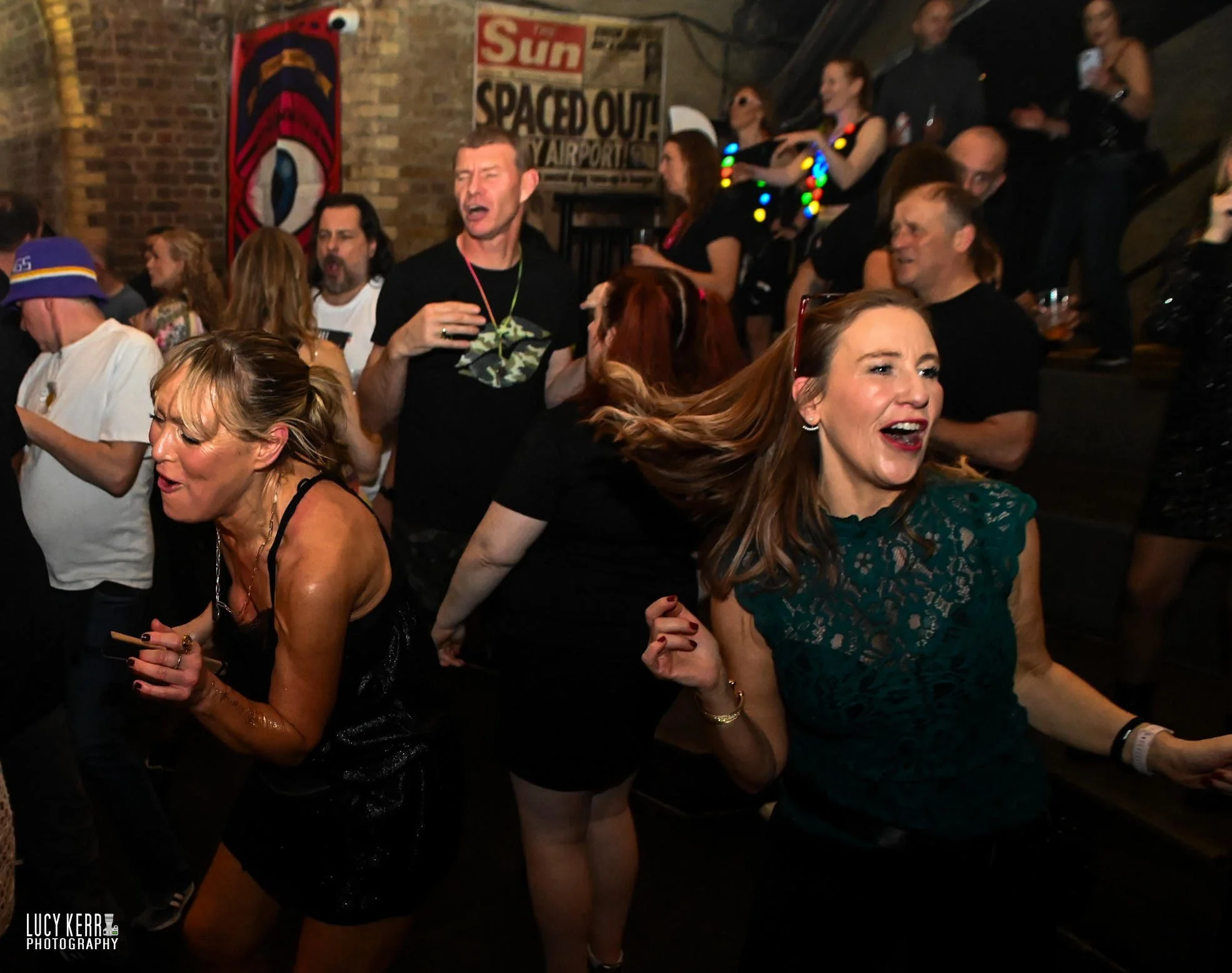 People dancing and enjoying themselves at a crowded Raindance party at Heaven Nightclub with a brick wall in the background.