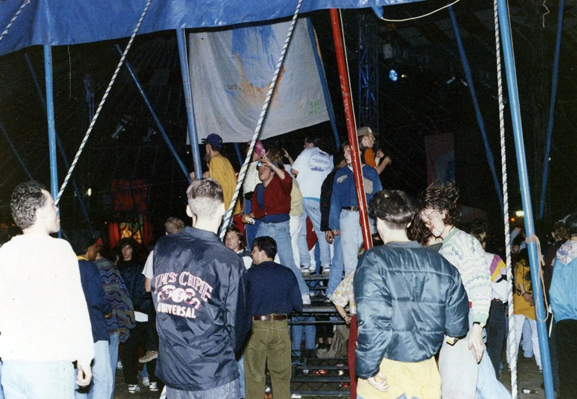 People gathered around a carnival swing ride at night, some standing and others on the ride.
