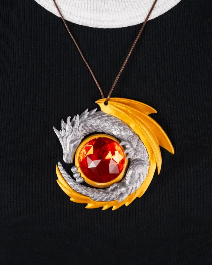 A necklace with a pendant featuring a silver dragon wrapping around a large red gemstone, with gold and black accents, worn on a black top.
