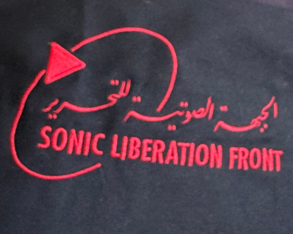 Red embroidered text and logo on black fabric, reads 'Sonic Liberation Front' in English and Arabic, with a stylized snake and triangle design.