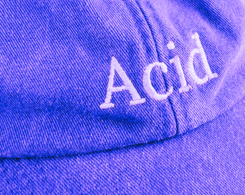 Close-up of a purple cap with white embroidered text 'A(cid)'.