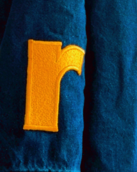 Close-up of a blue fabric with a yellow letter patch sewn onto it.