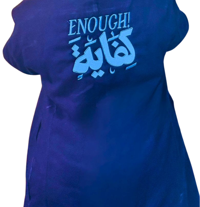 A person wearing a dark blue T-shirt with the words 'ENOUGH!' and Arabic script in light blue on the front.