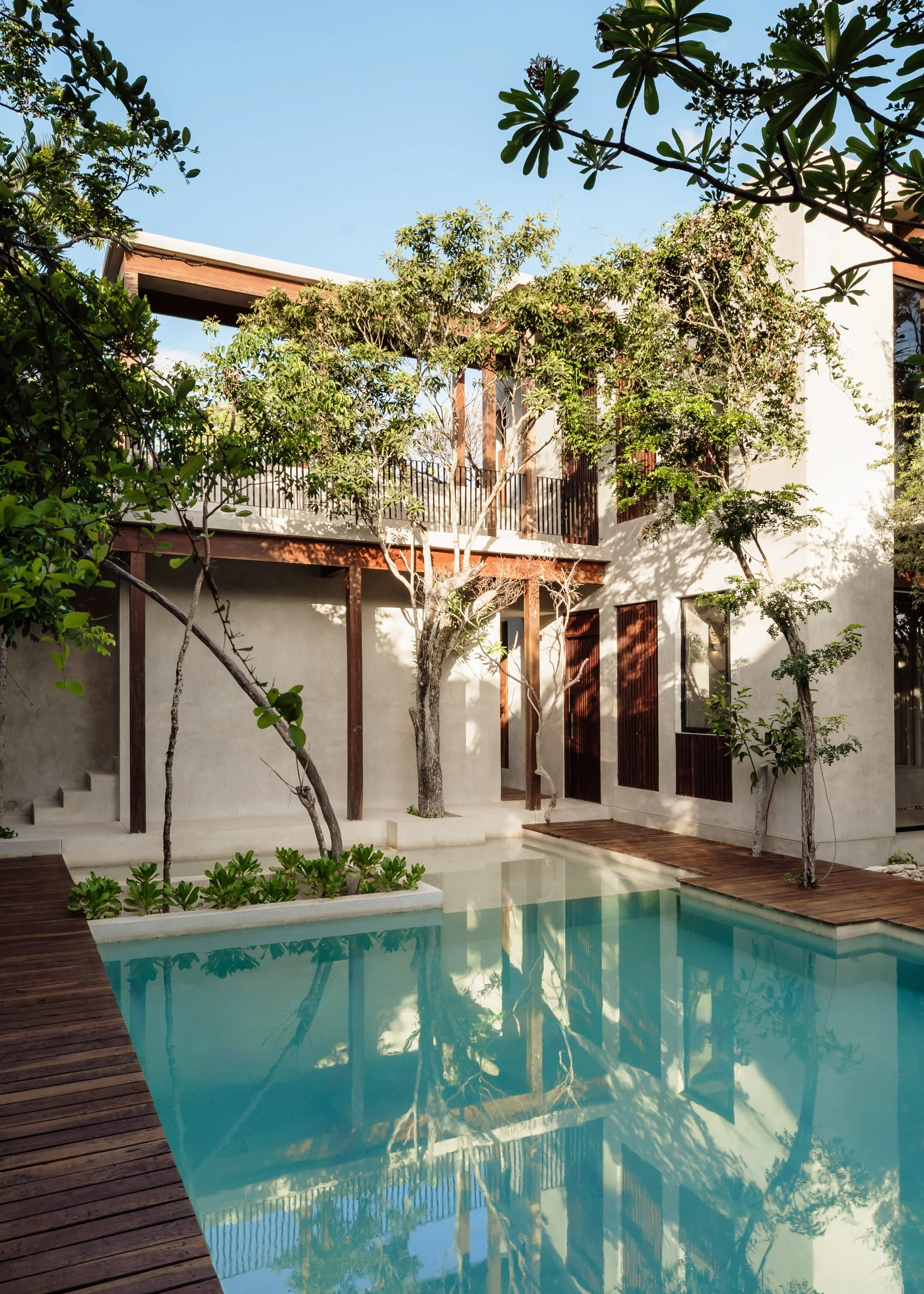 Modern house with a swimming pool, surrounded by greenery and trees, under a clear blue sky.