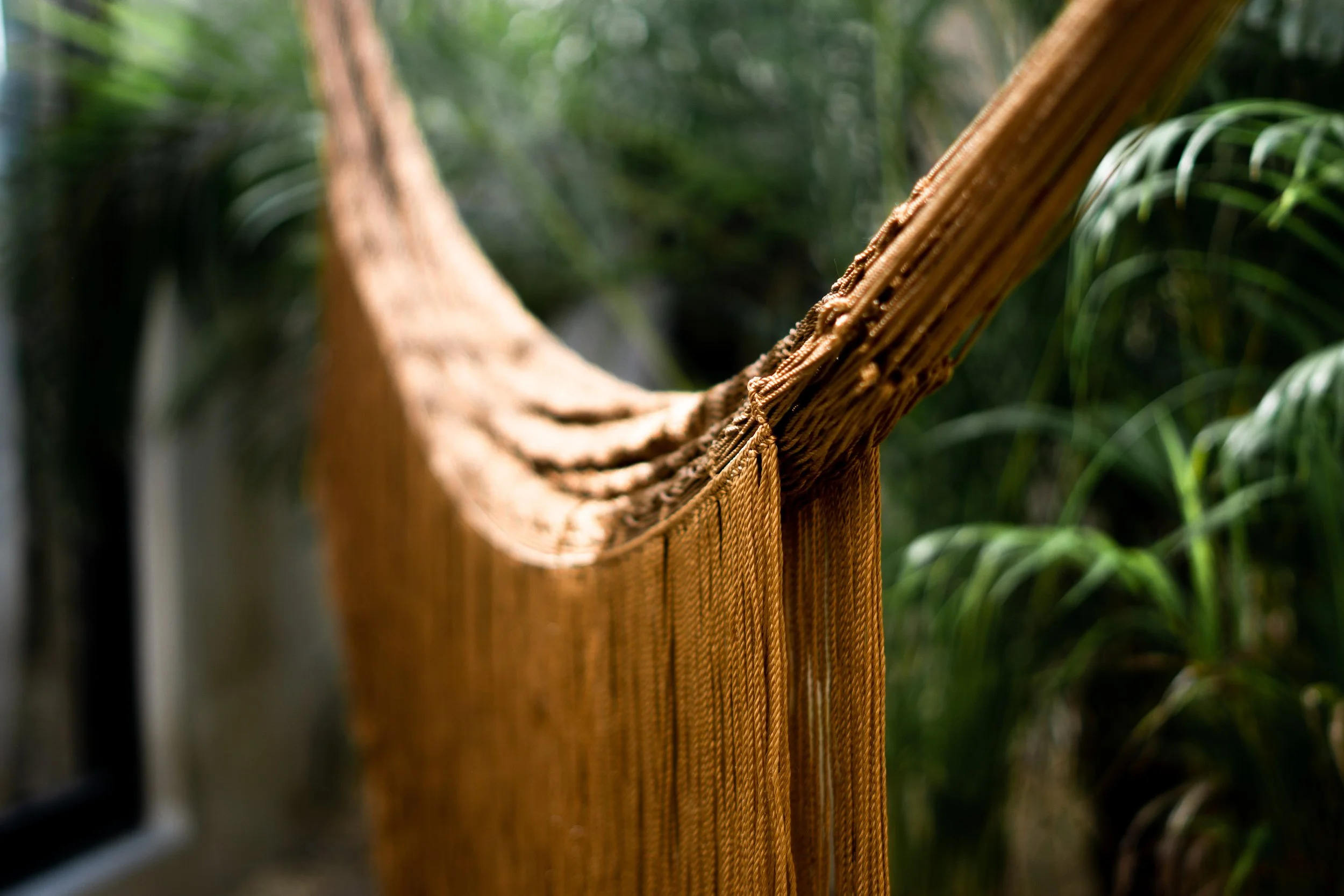 Close-up of a brown woven hammock hanging in a lush green outdoor setting.