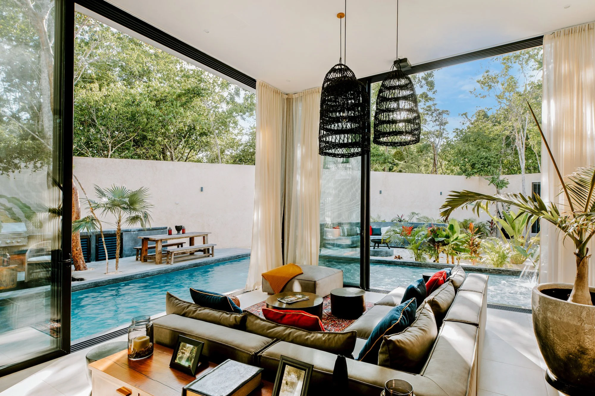 Living room with large glass doors open to outdoor patio and pool, with indoor plants and modern furniture.