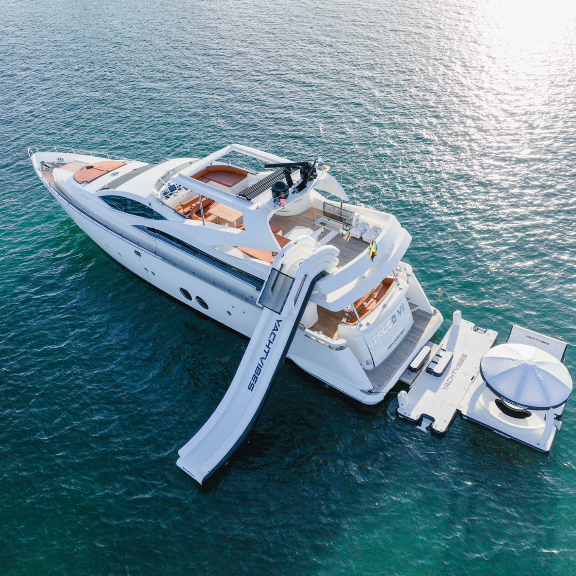 A large white yacht floating on the ocean with a spacious deck area, seating, and multiple outboard motors.