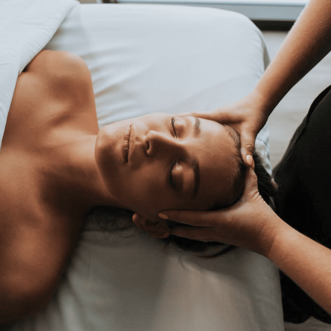 A woman receiving a professional massage on her head while lying on a bed.