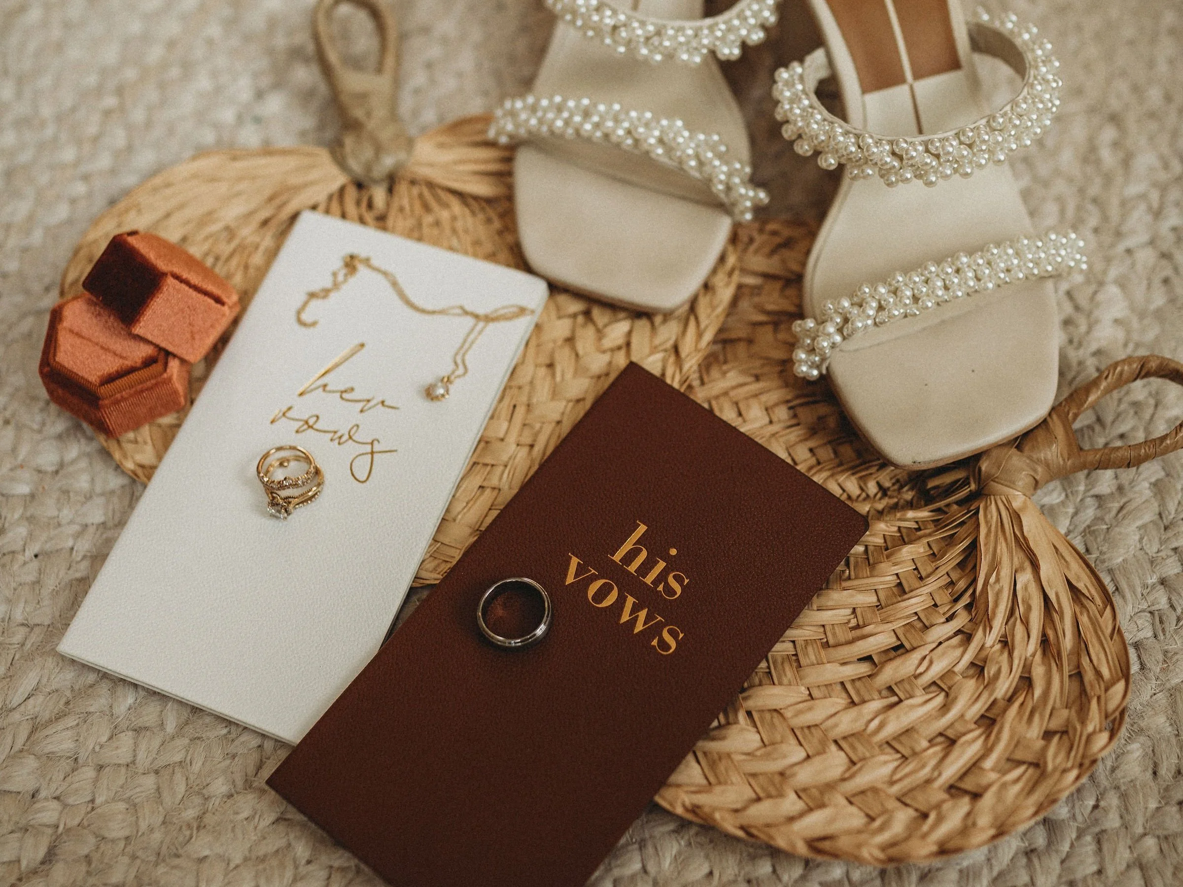 A woven basket containing various jewelry items and accessories, including pearl-embellished shoes, a jewelry card with a ring, a gold necklace, and a small decorative box, placed on a textured surface.