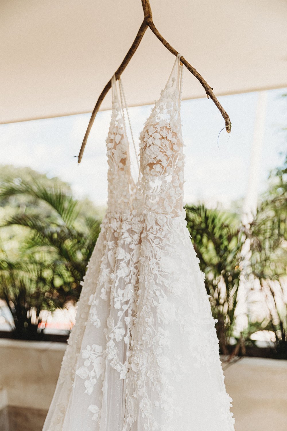 A white, lace wedding dress hanging from a tree branch outdoors.