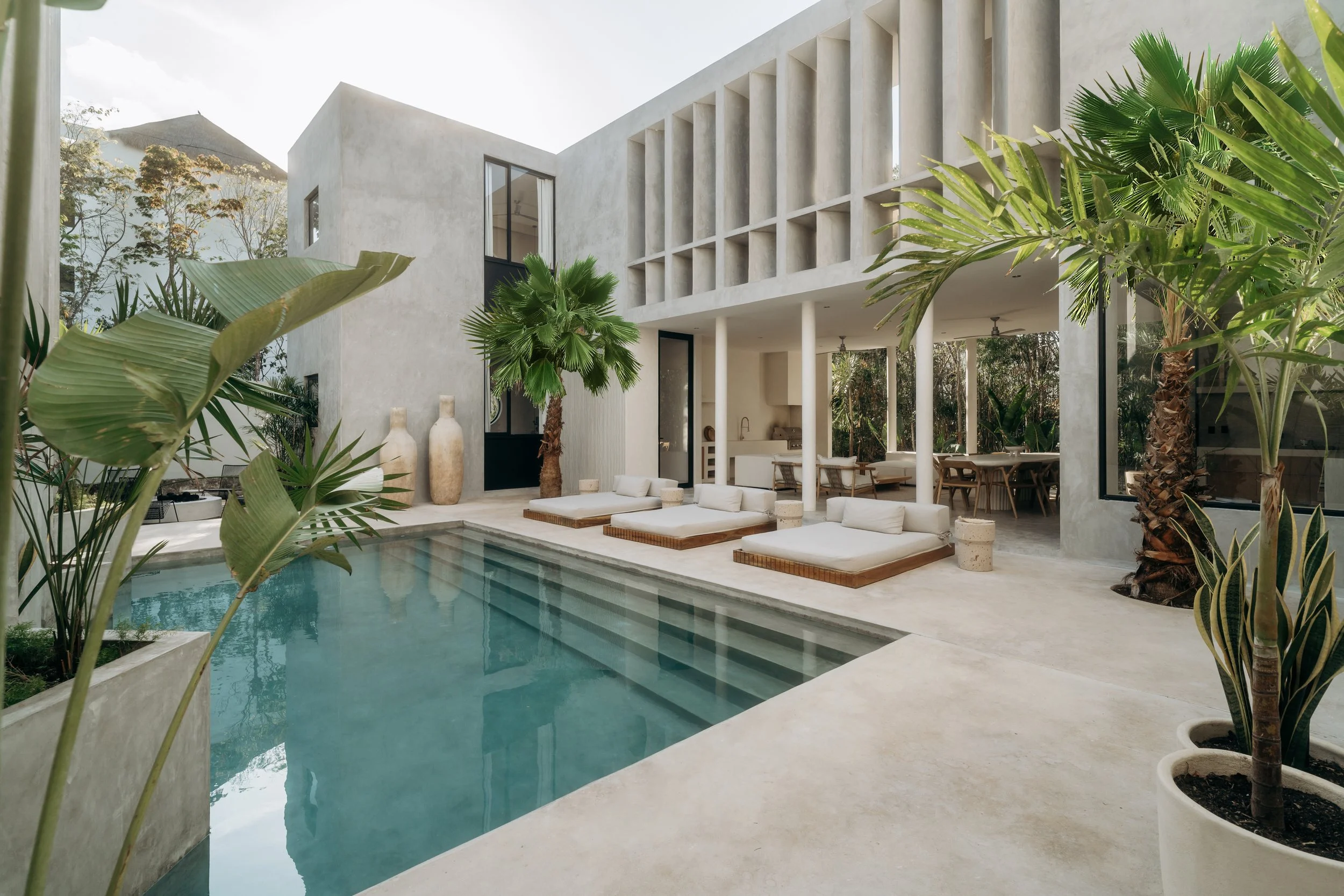 Modern house with pool and outdoor lounge area, surrounded by tropical plants.