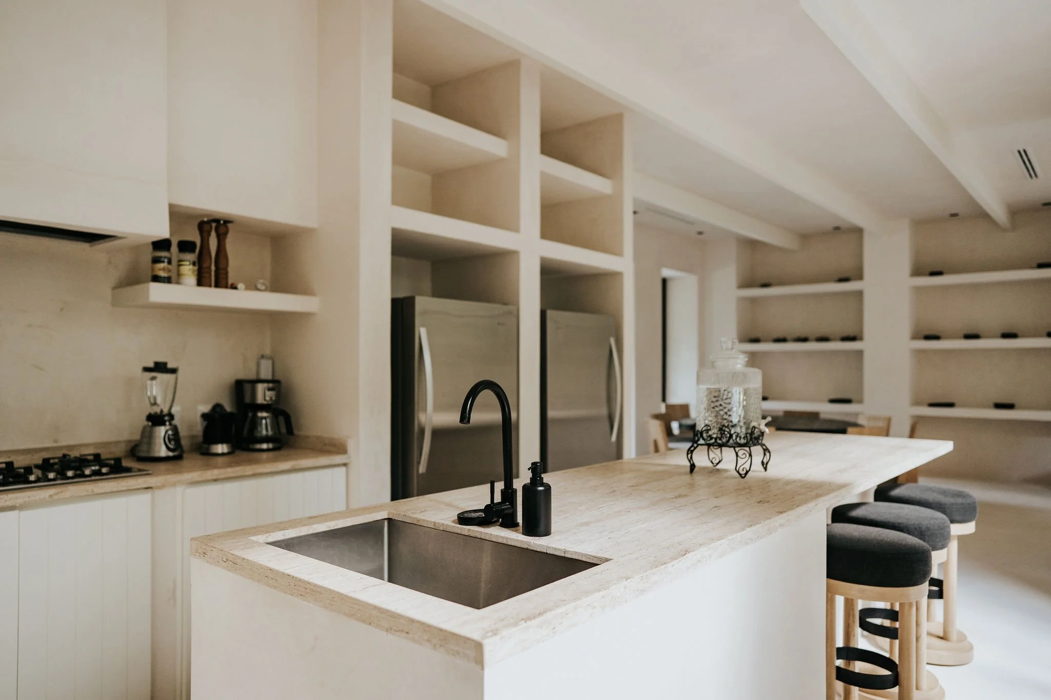 Modern kitchen with white cabinets, open shelving, a kitchen island with seating, black faucet, and stainless steel appliances.
